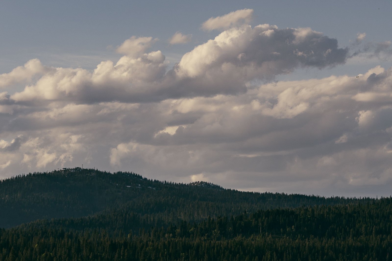  Clouds fill the sky above forested hills, with sunlight casting soft shadows over the landscape. The scene has a tranquil, natural atmosphere. 