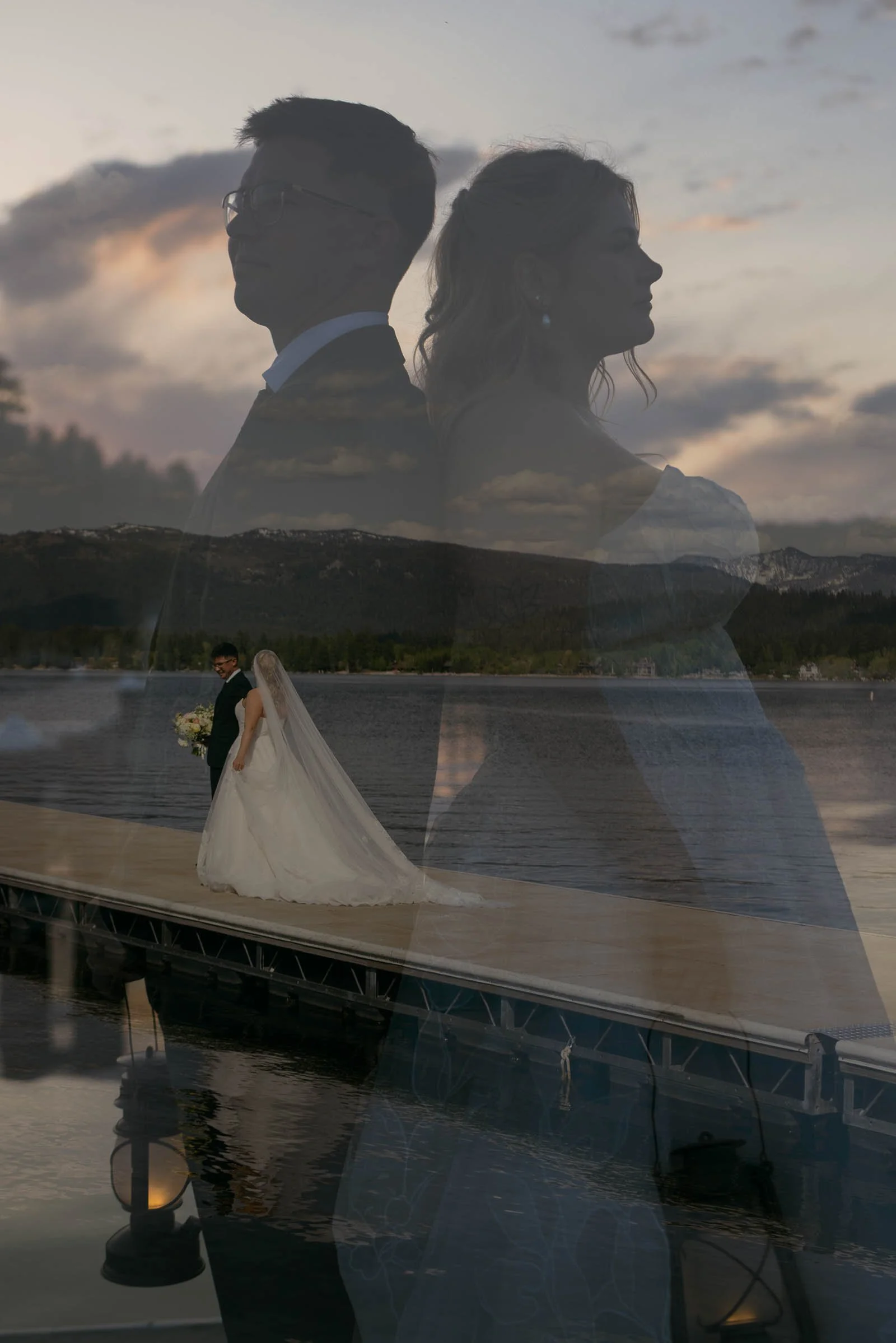 A double-exposure portrait layers a bride and groom standing back to back over an image of them walking a lakeside dock, mountains and overcast sky behind.