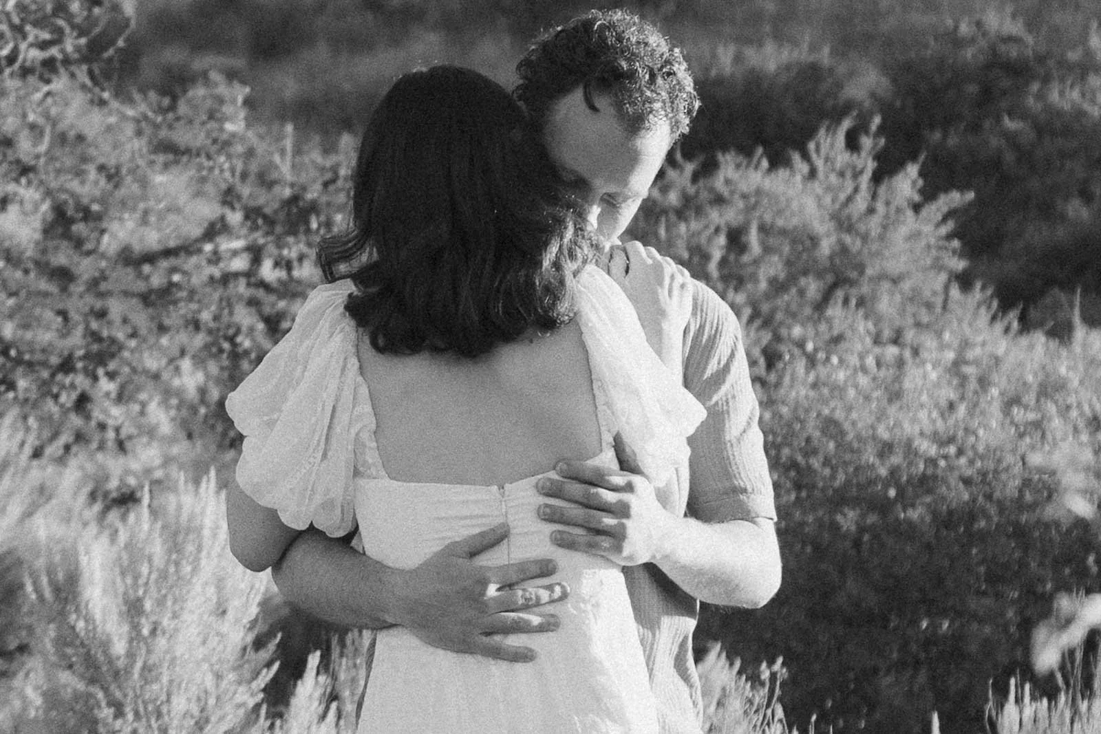  A couple embraces outdoors in a grassy field. 