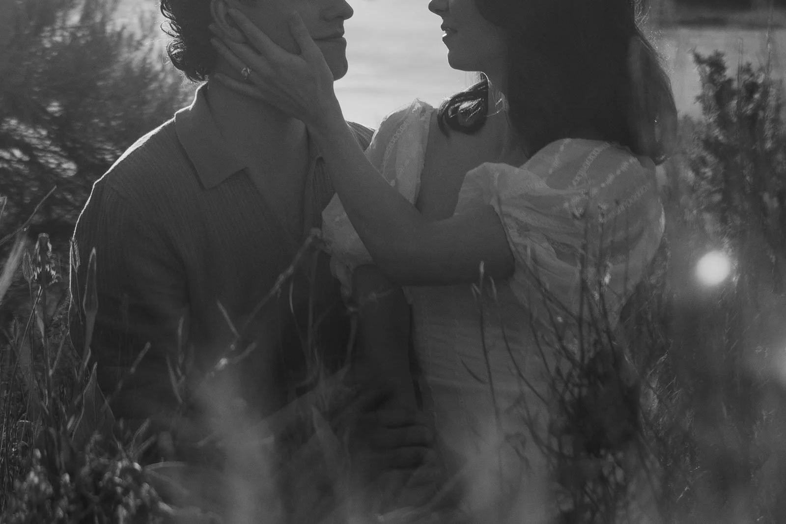  A woman touches a man’s face as they look at each other in a grassy field. 