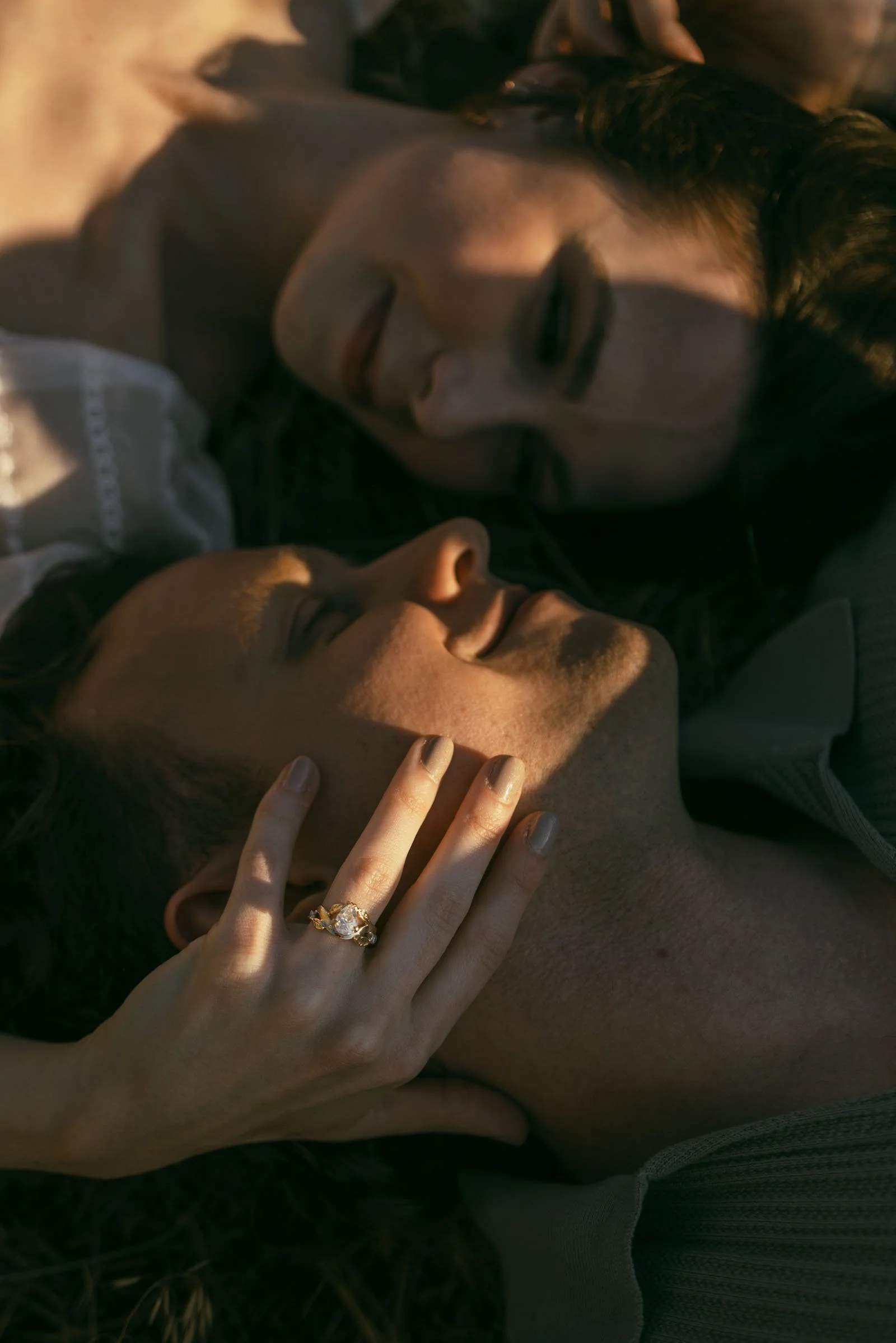  A person gently touches their partner’s face, showcasing a gold ring with a clear stone on their finger. 