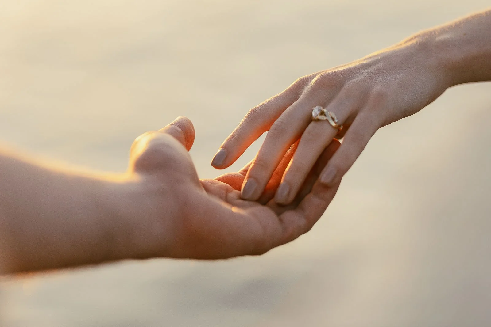 Close-up of a gold engagement ring as a bride-to-be rests her fingers in her fiancé’s open palm, glowing in warm sunset light at Lucky Peak near Boise, Idaho.