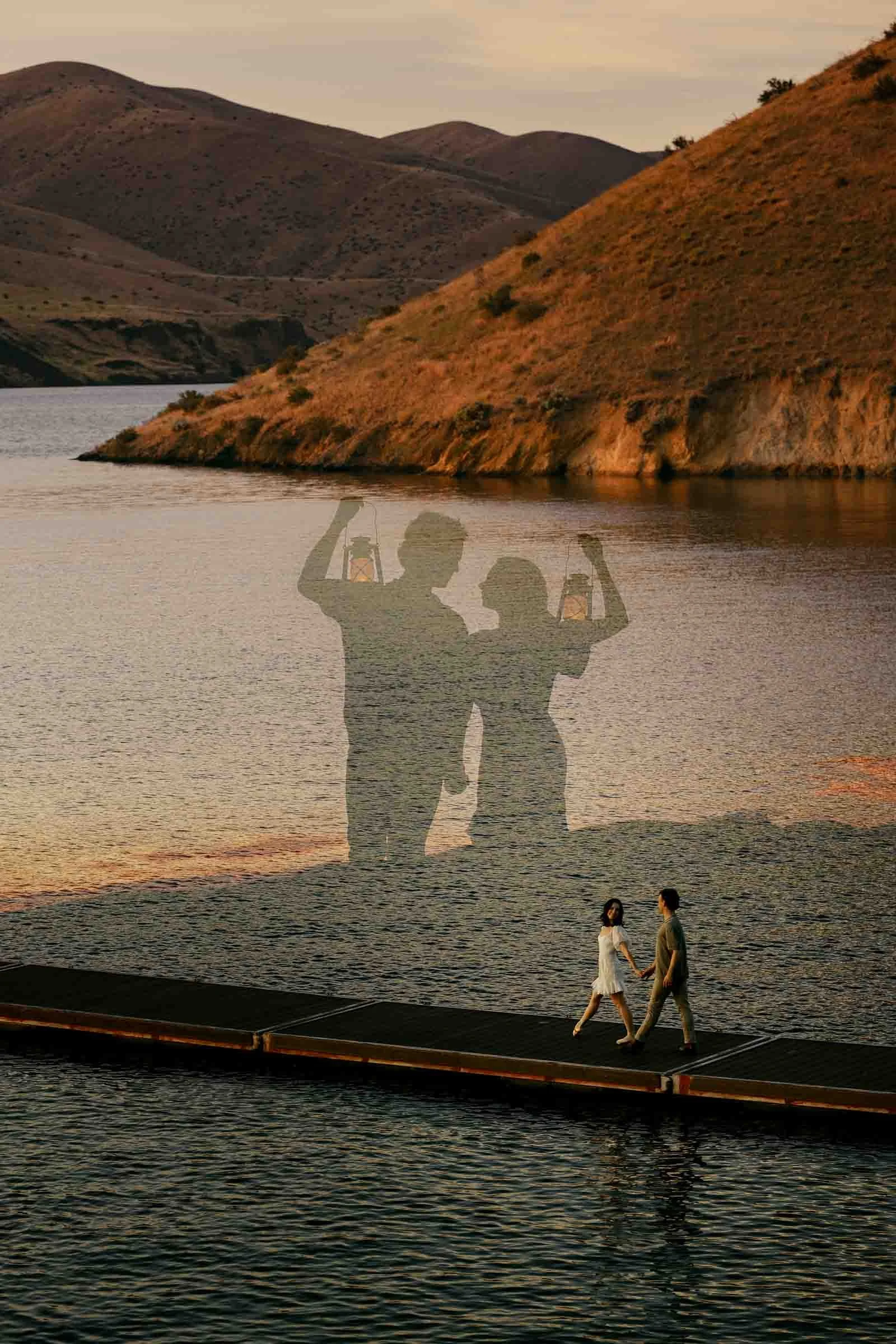 Fine art double exposure of an engaged couple raising lanterns, blended over the two of them walking hand in hand on a floating dock at Lucky Peak at sunset.