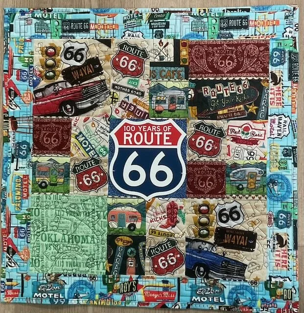 Route 66 Mixed Media
by Nantelle Kemp
*
Patchwork quilt of various Route 66 fabrics with the addition of a 3D printed Route 66 medallion.  Machine pieced and quilted on Baby Lock Solaris. Quilting features cars and trucks.