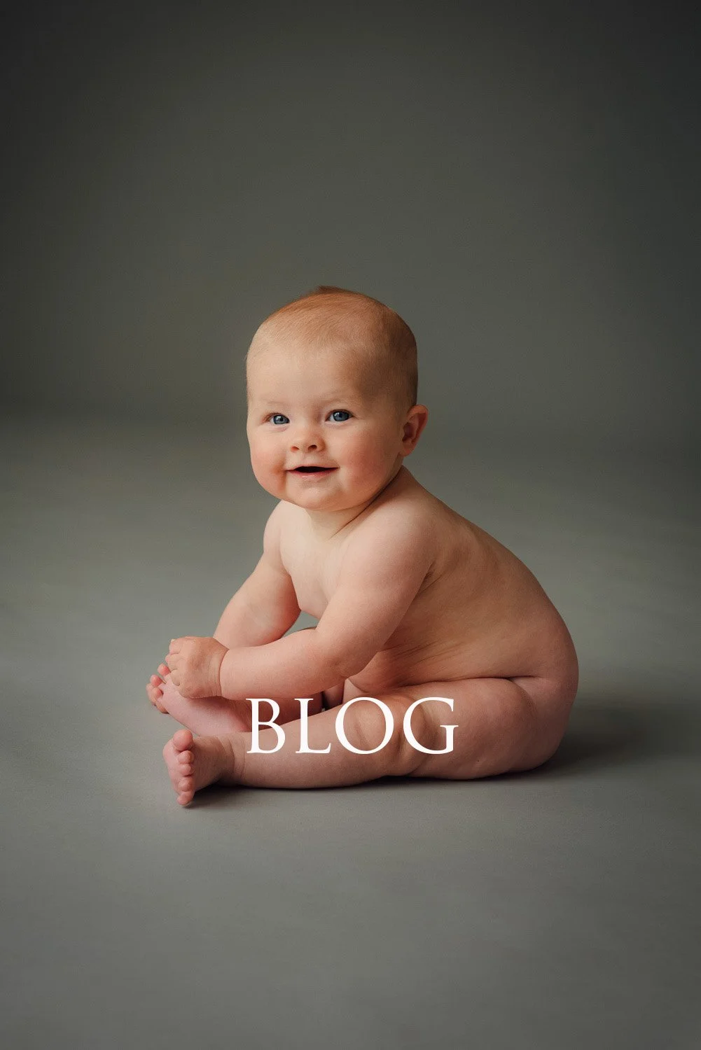 Chubby baby sitting on a gray floor, smiling, with the word 'BLOG' overlaid at the bottom.
