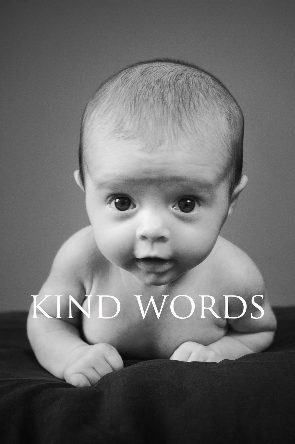 Black and white photo of an infant with big eyes, looking up, with the words "KIND WORDS" overlaid.