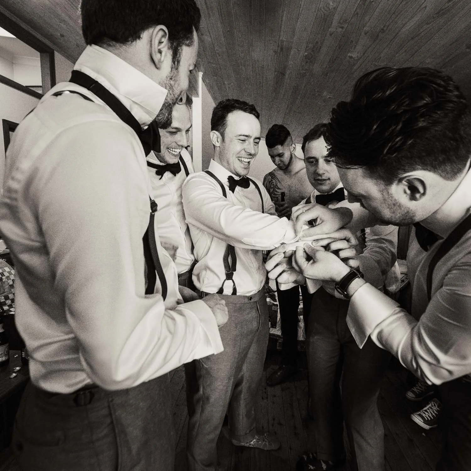Groomsmen helping groom to get ready with cufflinks black and white photo wedding photo