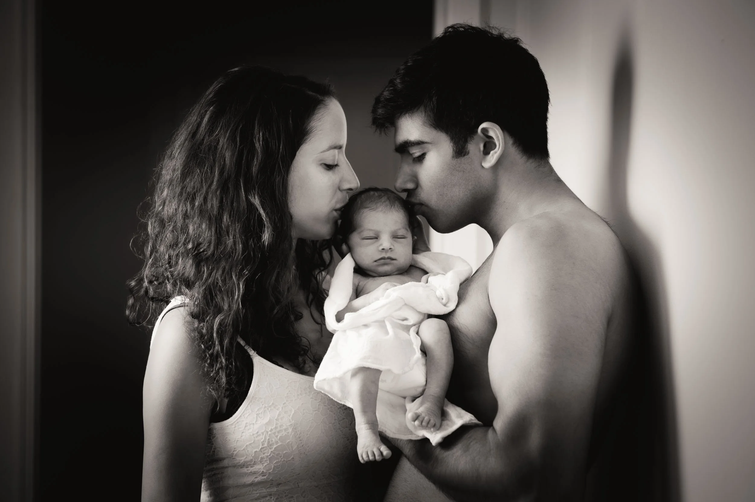 parents kissing while holding their baby between them for a newborn photoshoot