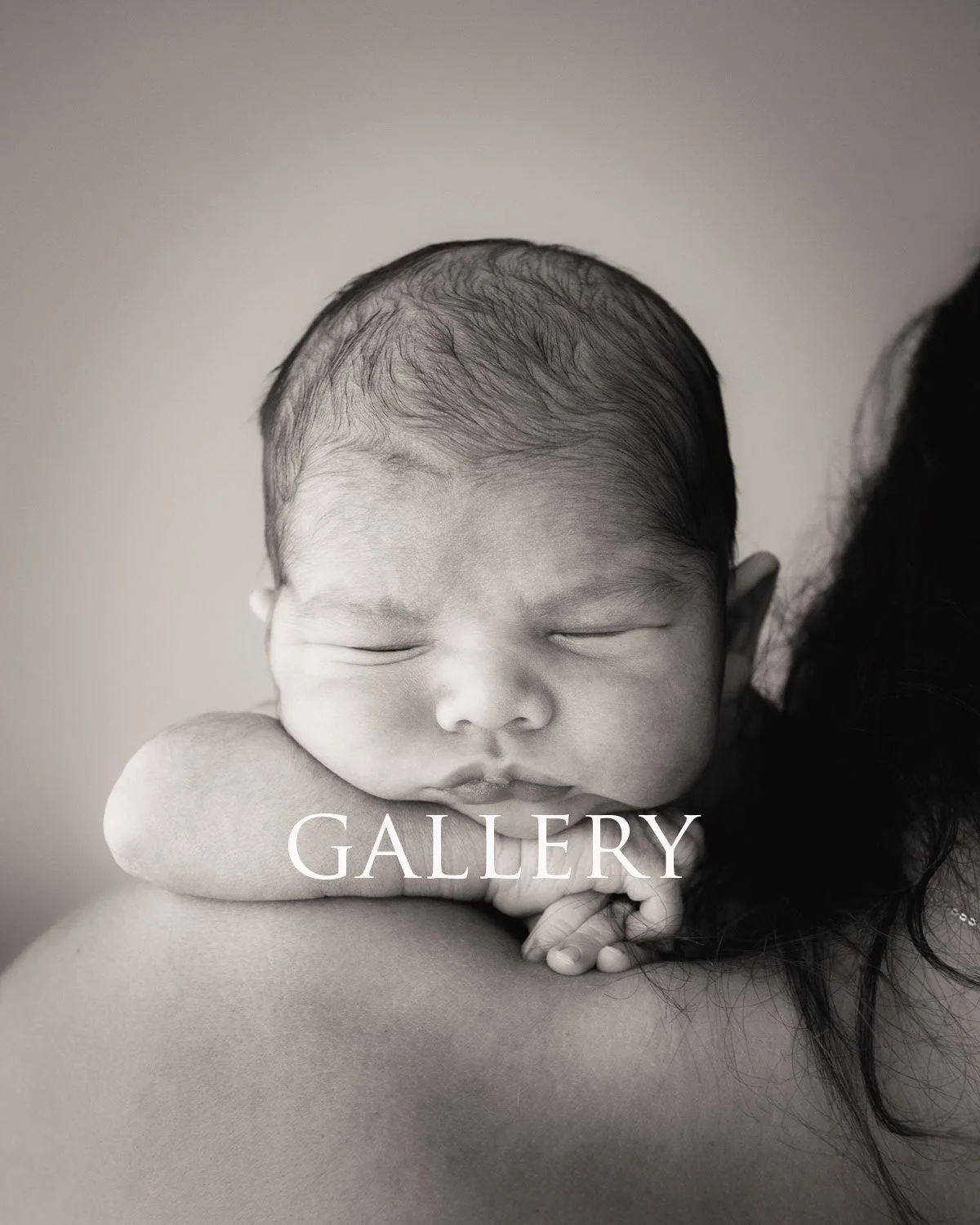 Black and white photo of a sleeping baby resting on an adult's shoulder with closed eyes and relaxed face.