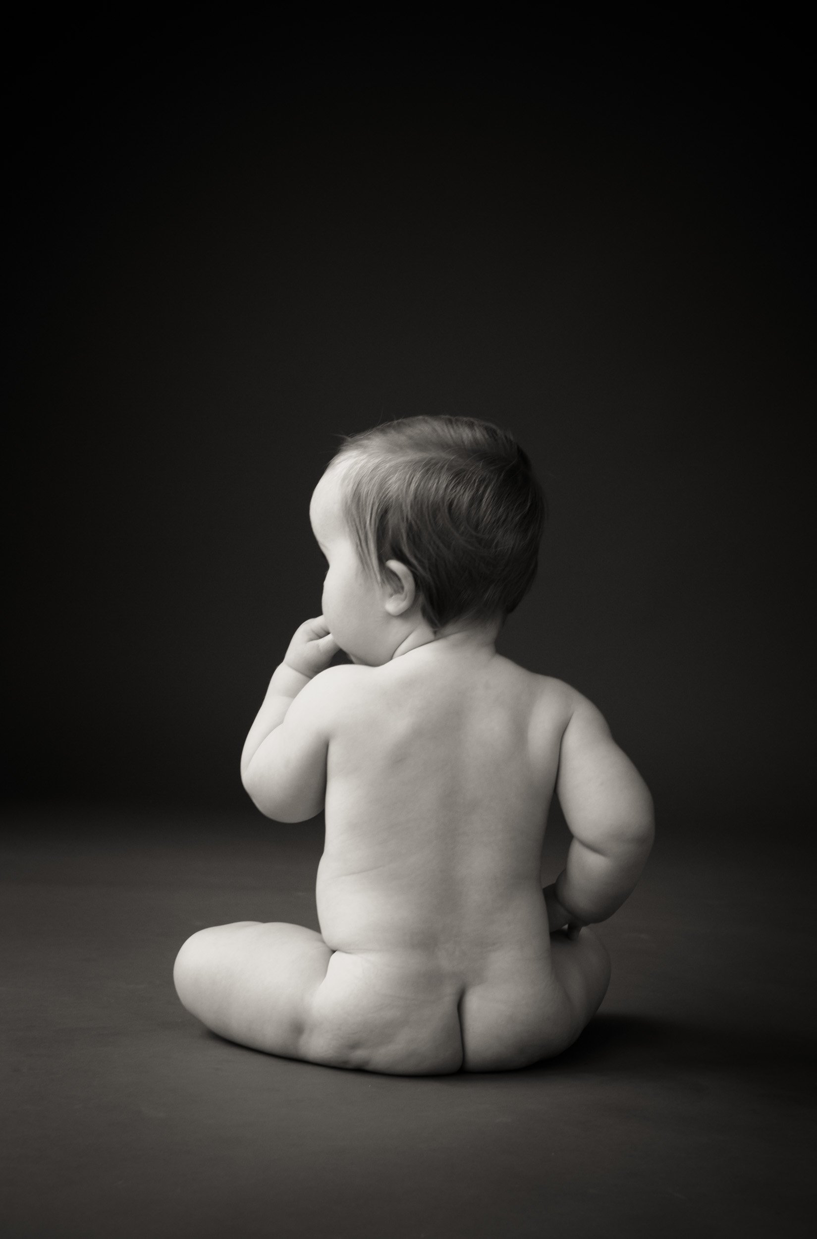 studio baby photoshoot of back of nude baby sitting on background