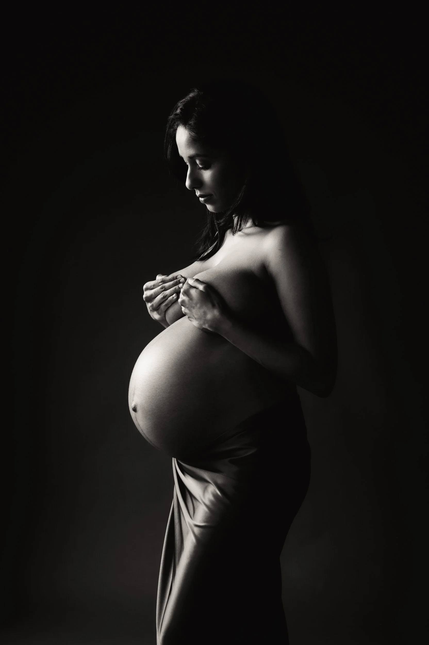 beautiful maternity portrait of a woman holding breasts with moody lighting