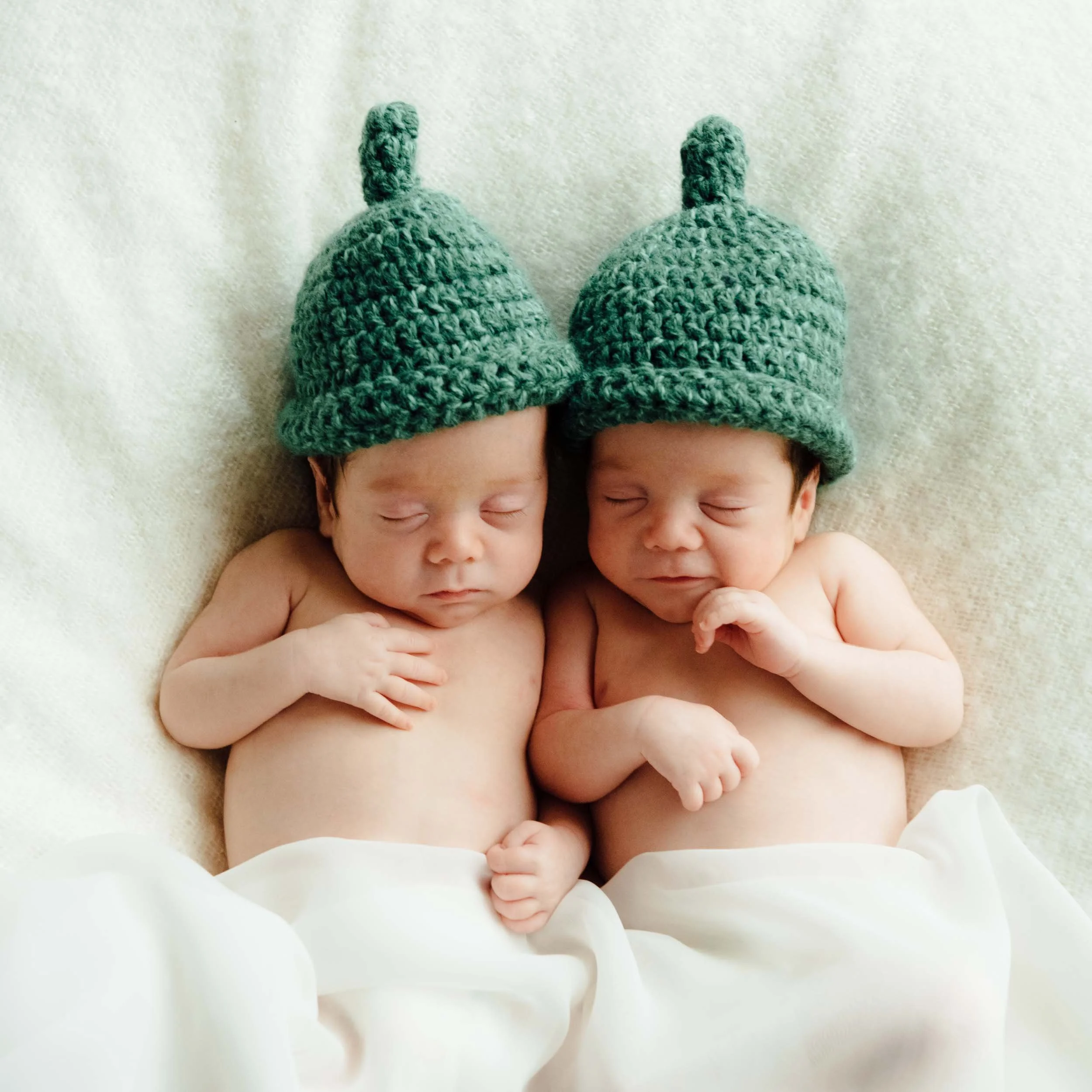 twin newborn photography of sleeping babies wearing green knitted hats