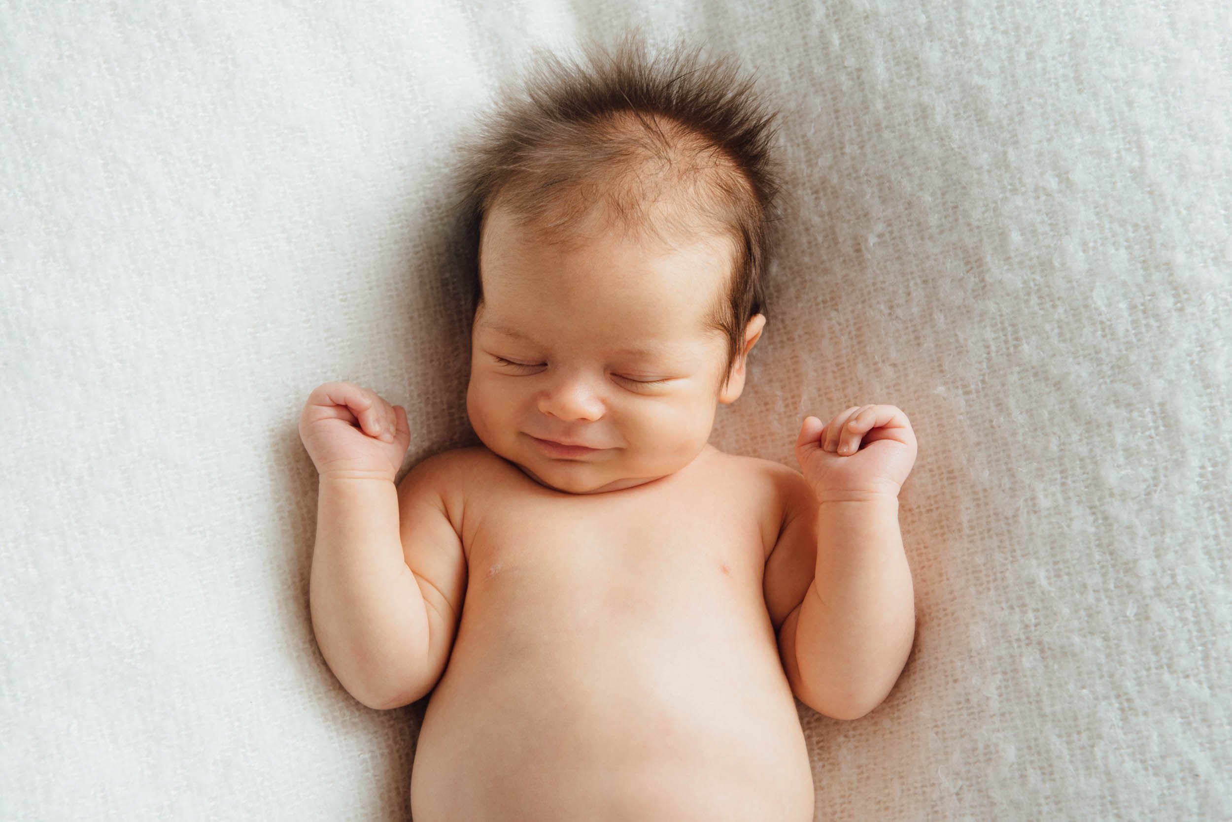newborn with eyes closed and smiling
