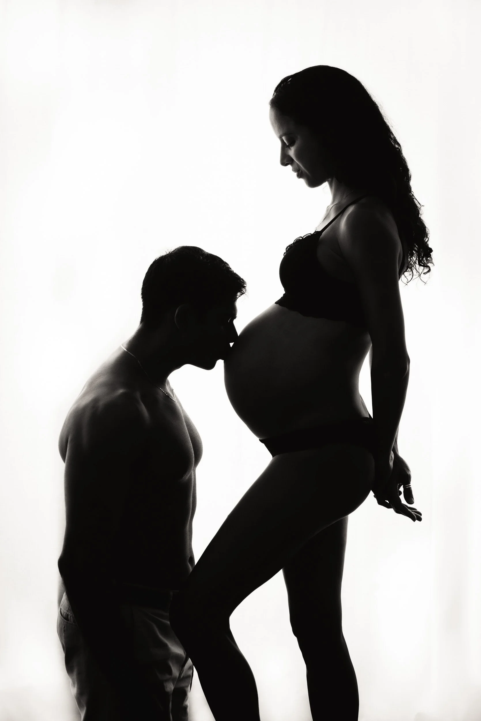 silhouette of man kissing pregnant wife's belly during a maternity photoshoot