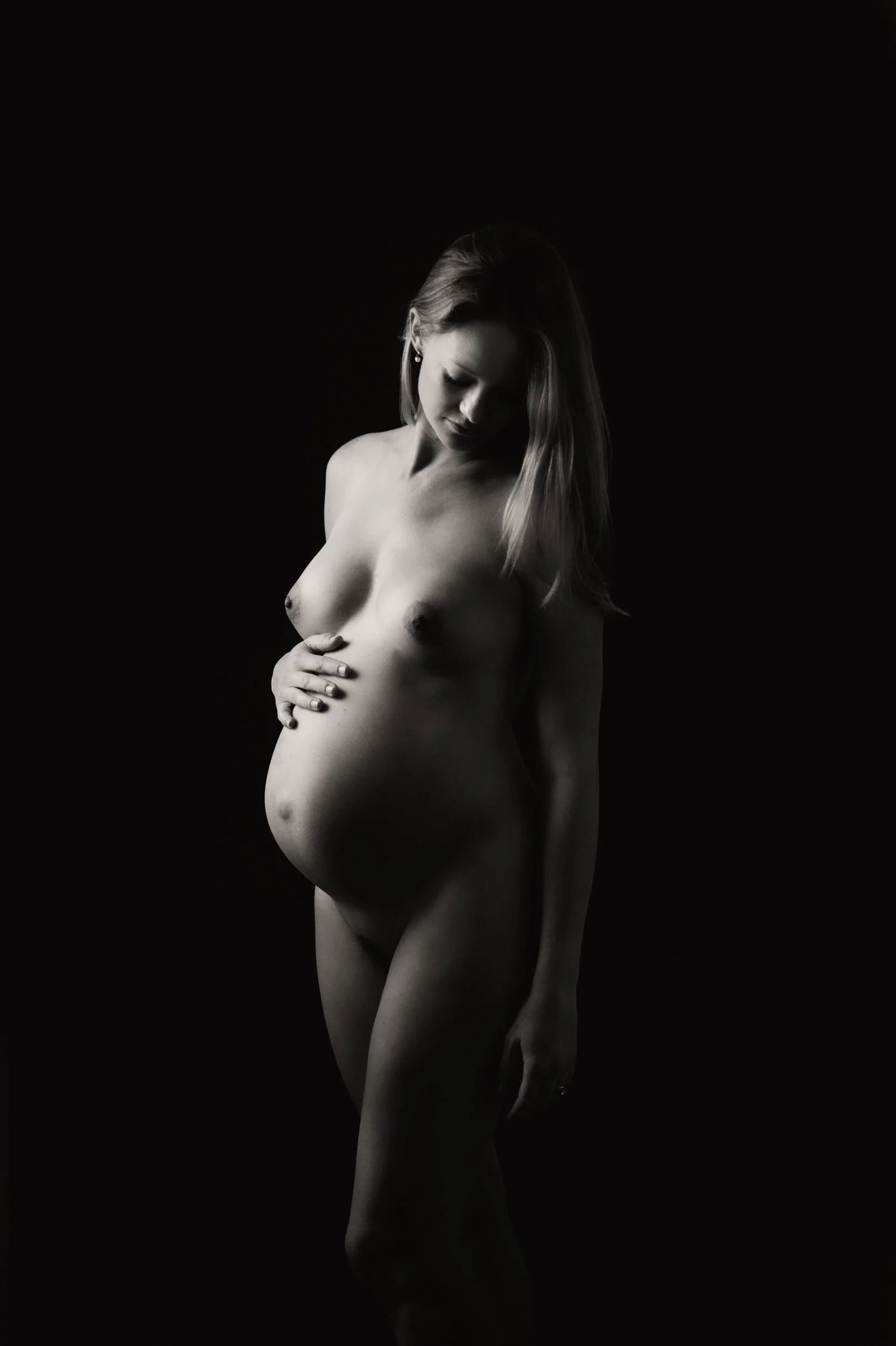 Maternity photoshoot of a woman in moody lighting looking down