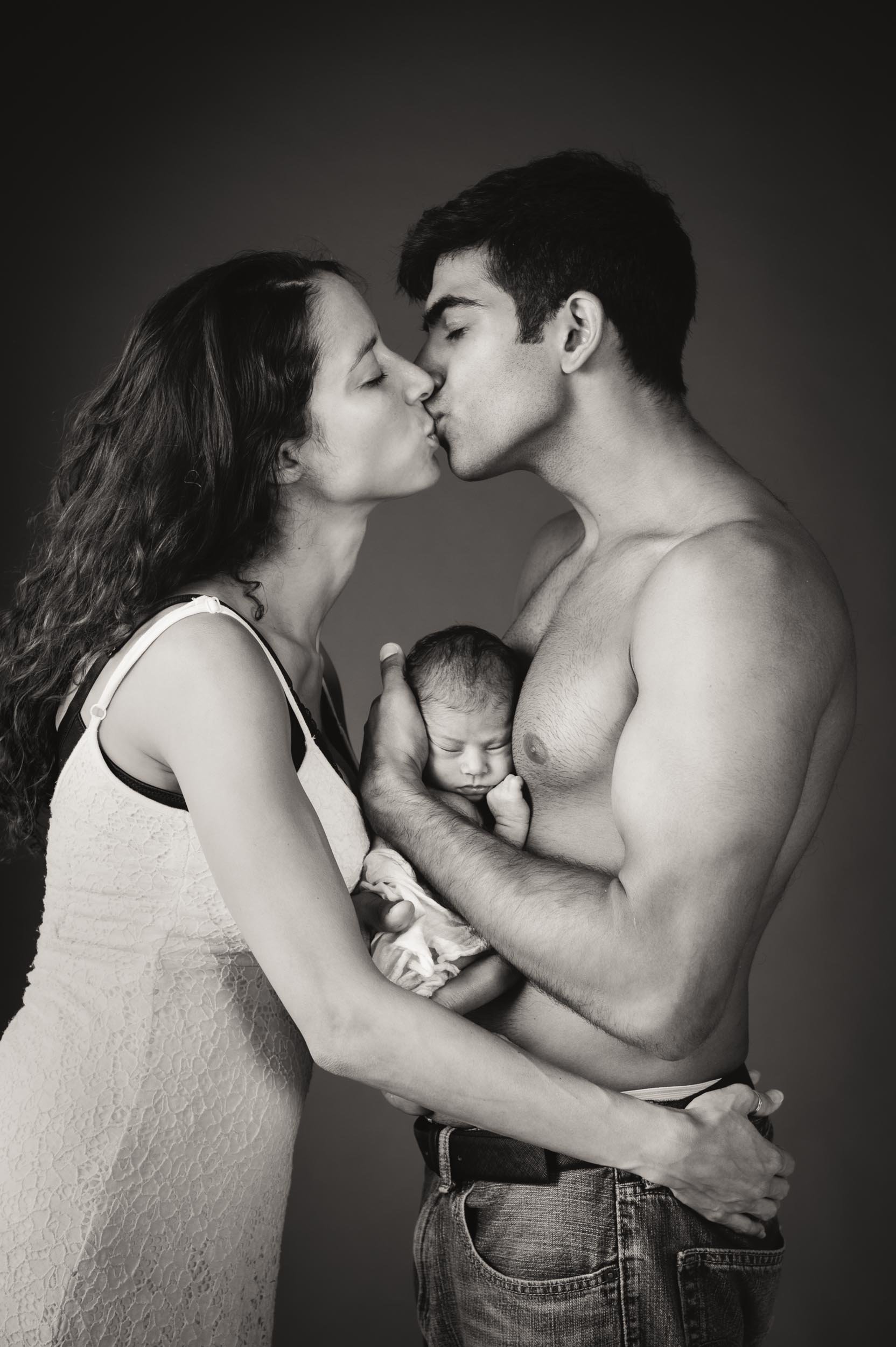 parents kissing while holding their newborn between them