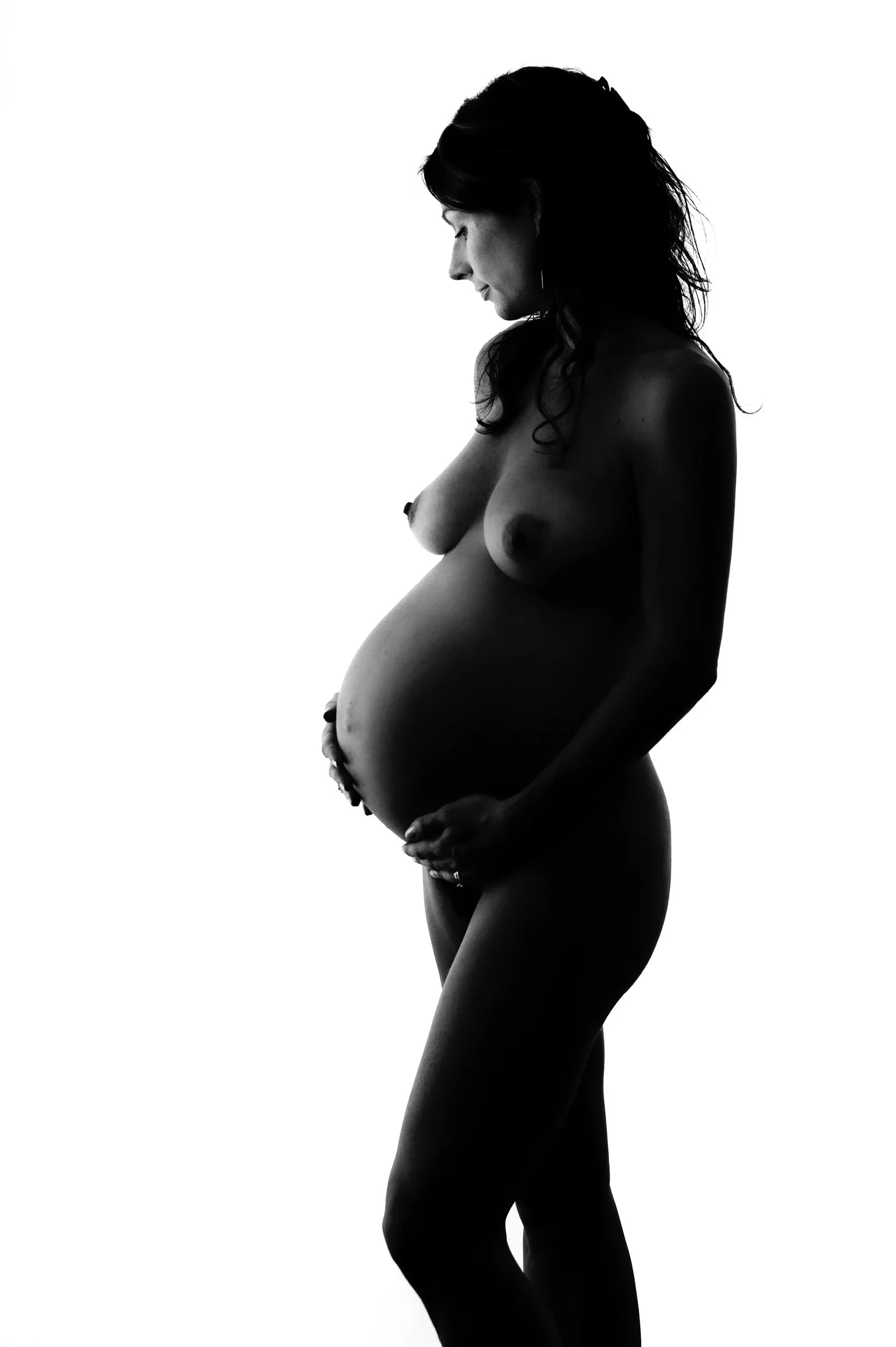 Elegant nude maternity photoshoot of a woman holding her belly in silhouette