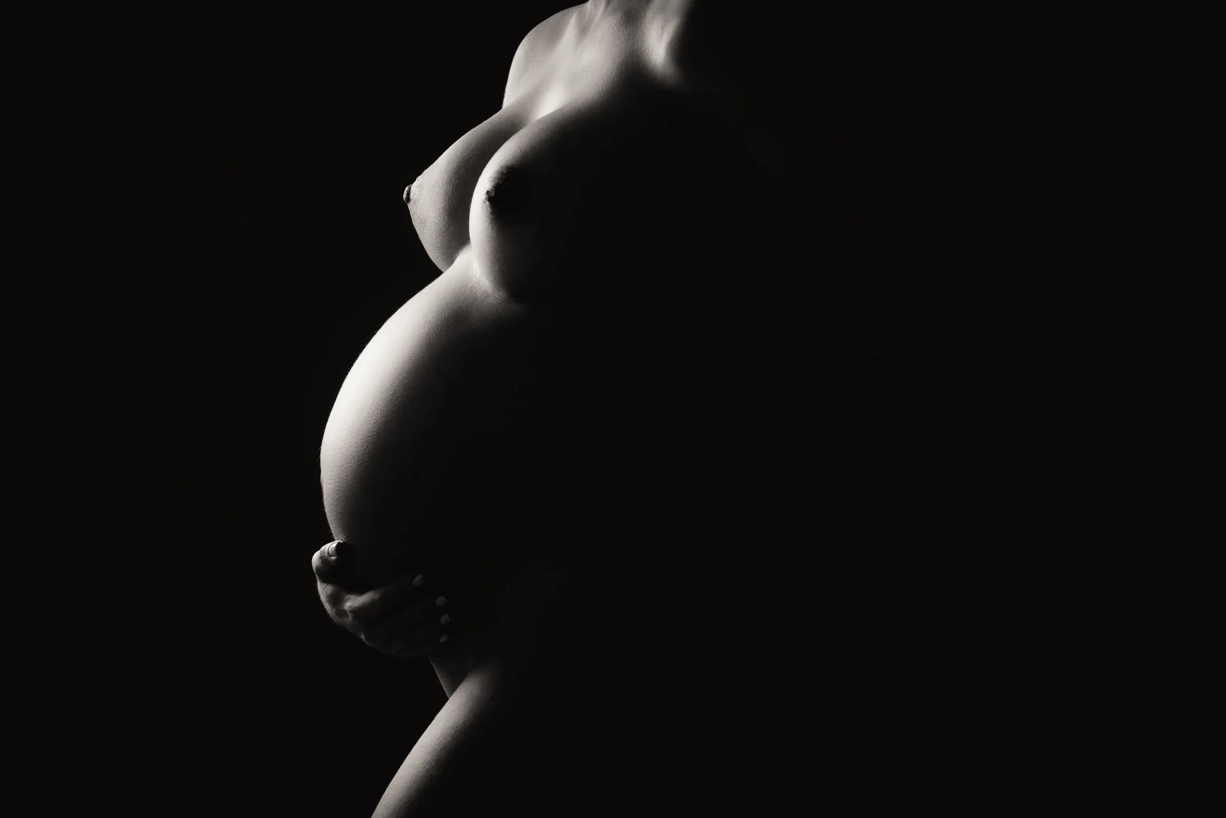 Maternity photography of a big belly close-up back lit