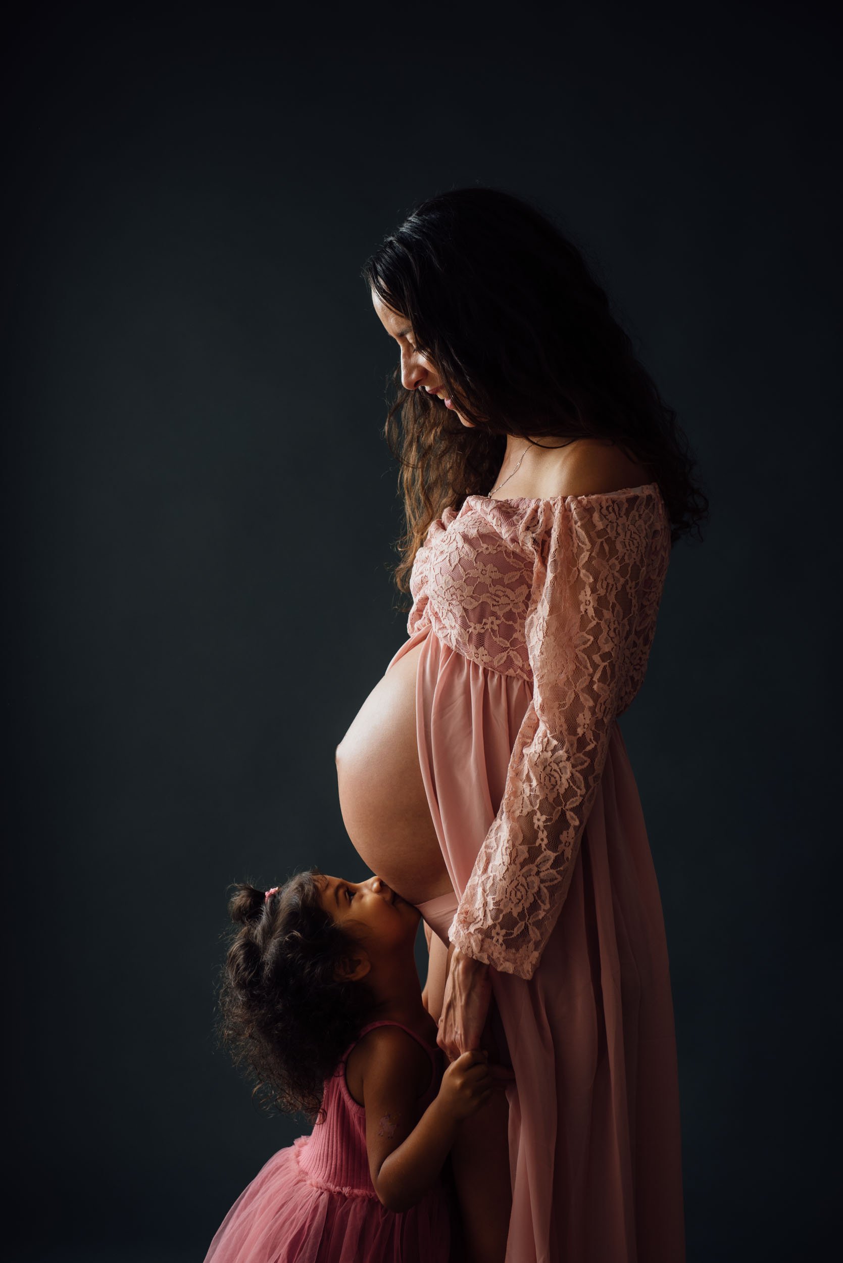 Daughter kissing her mother's pregnant belly during a maternity photoshoot