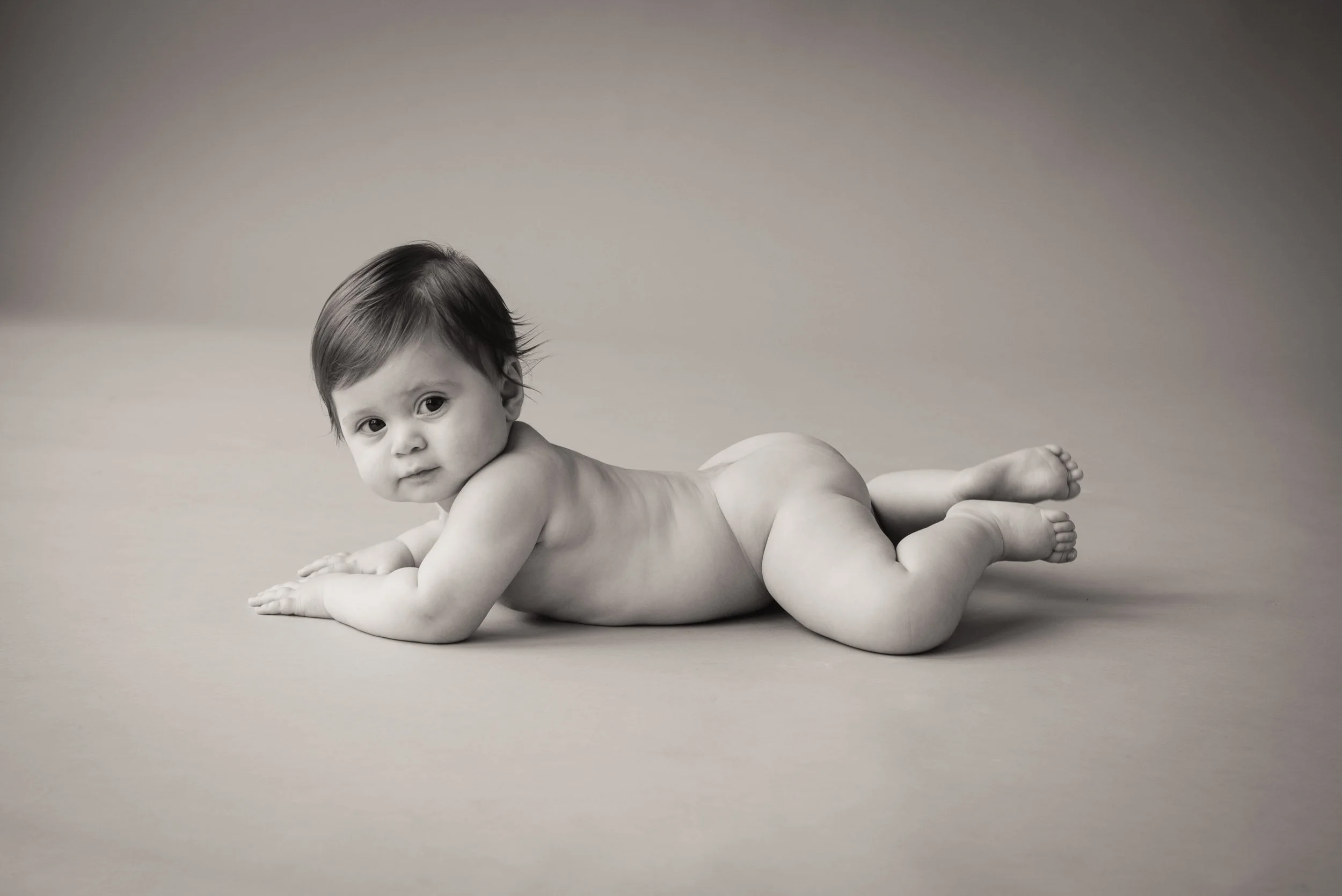studio baby photoshoot of 6 month old girl lying on background