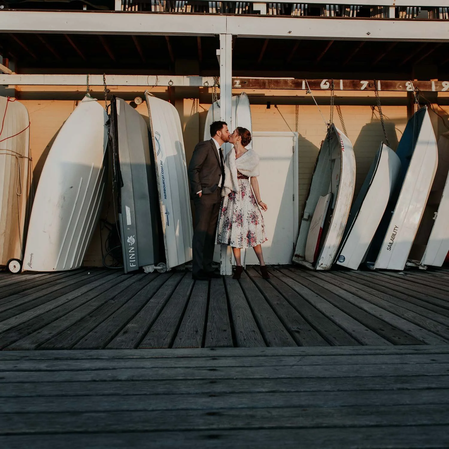 bride with unusual wedding gown kissing groom in golden light with dinghies in the background 