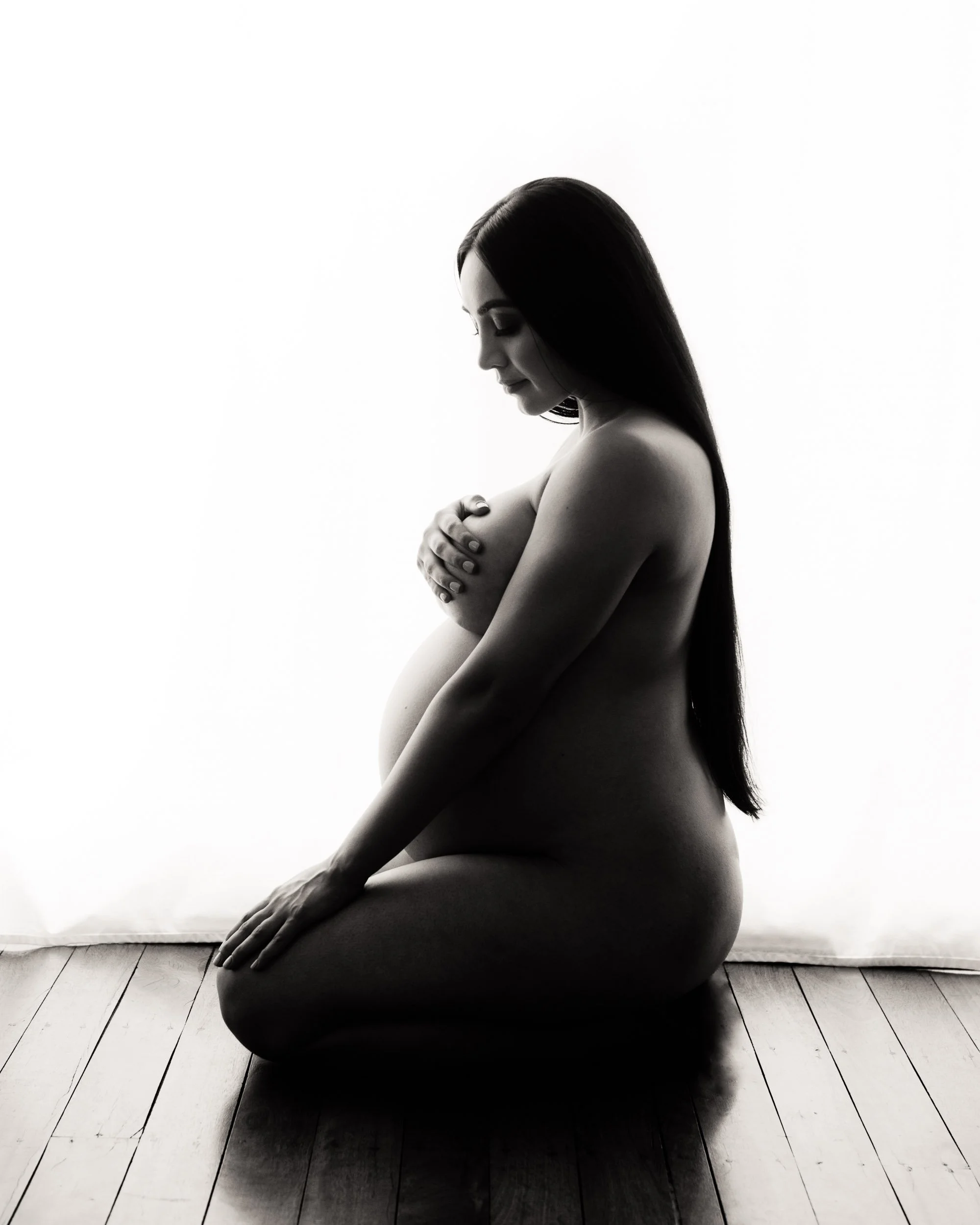 Silhouette maternity photoshoot of a woman sitting on the floor.