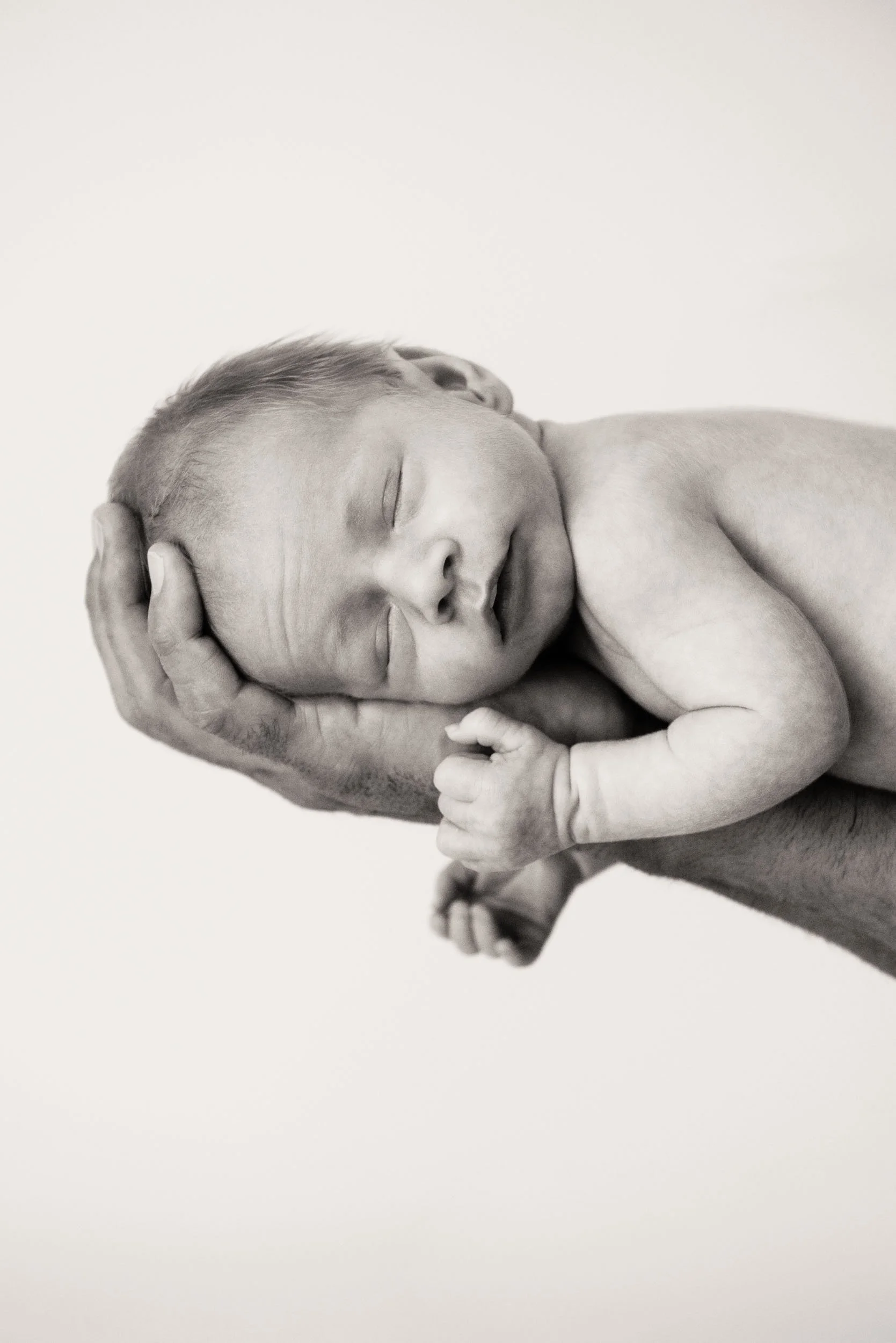 Newborn photoshoot of sleeping baby in dad's hands in black and white