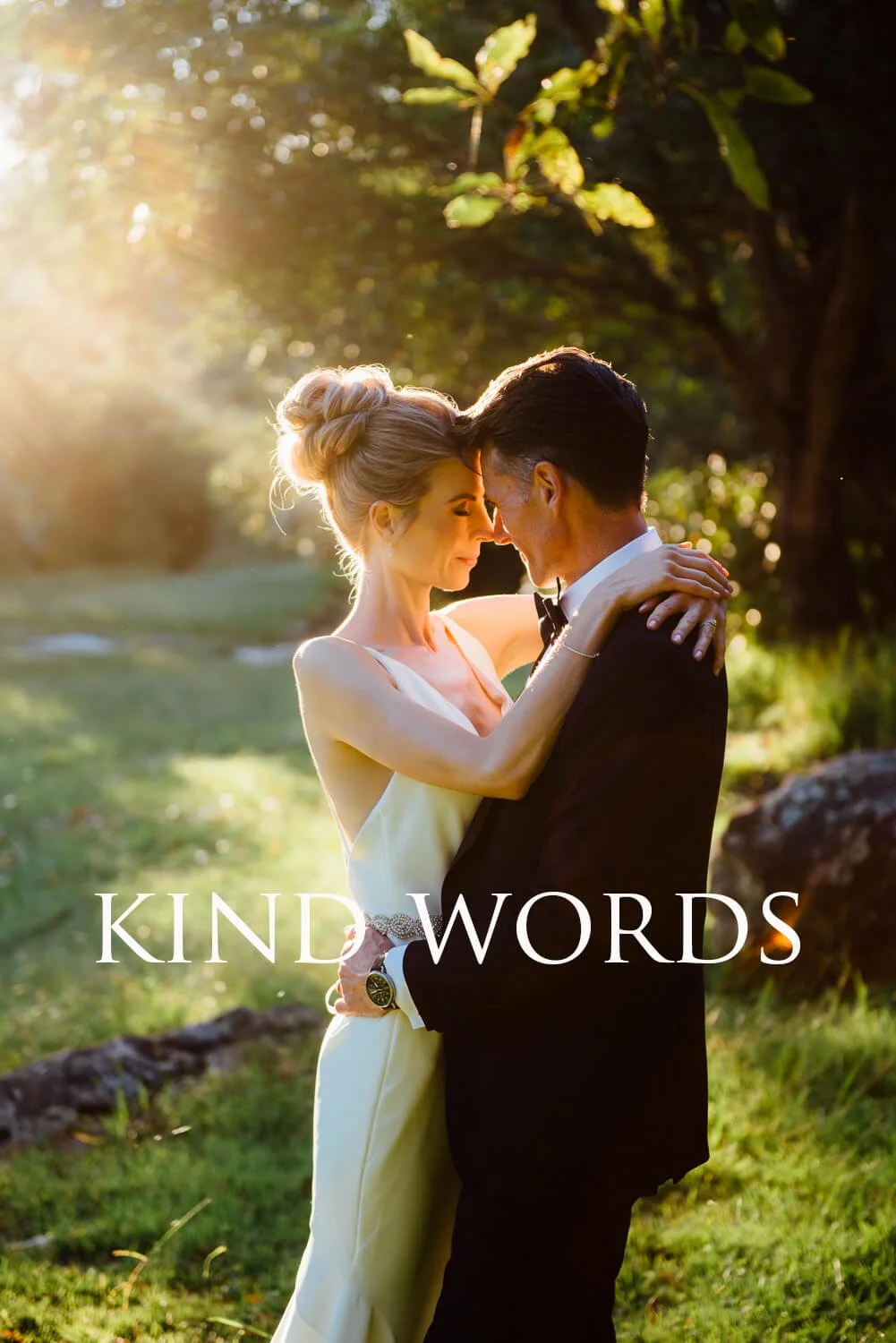 A couple dressed in formal attire embracing outdoors during sunset, with the words "KIND WORDS" written on the image.