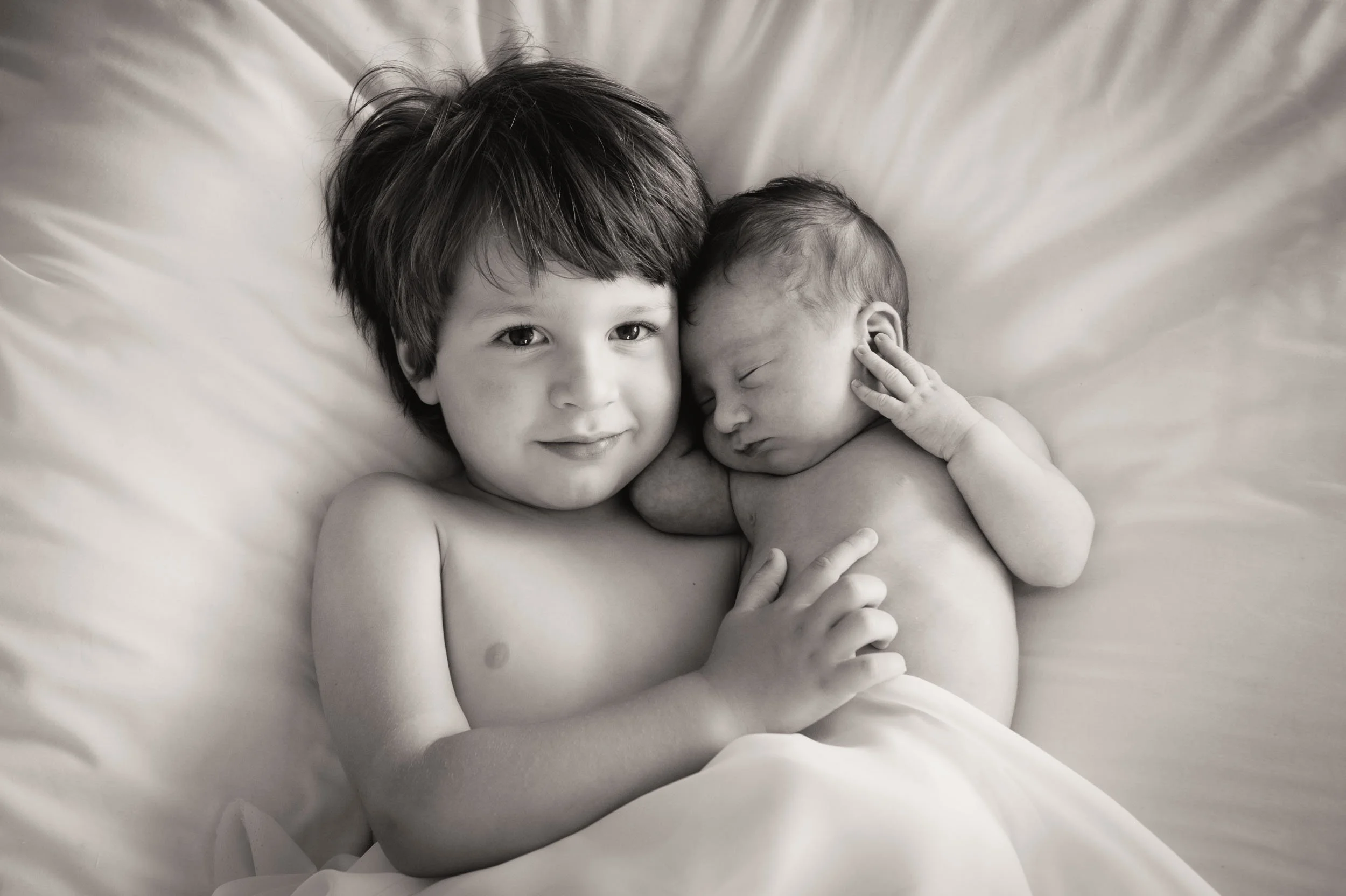 Newborn with older brother cuddling in bed