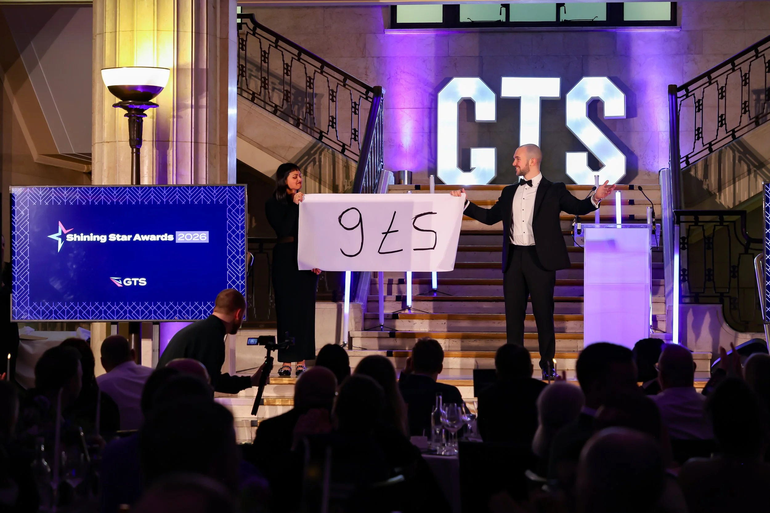 A magician working closely with a volunteer on stage as the audience reacts with excitement.