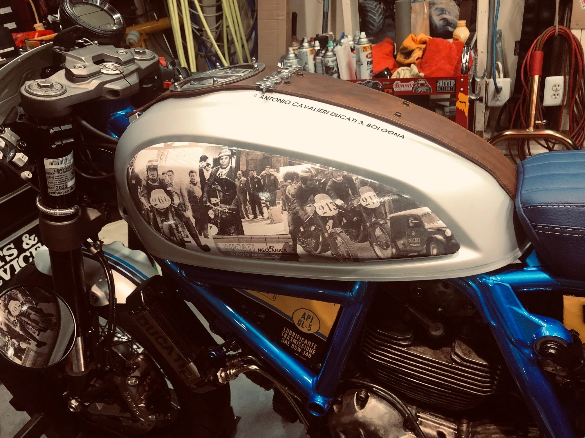 Custom Ducati motorcycle with vintage-themed graphics on fuel tank, surrounded by workshop tools and equipment.