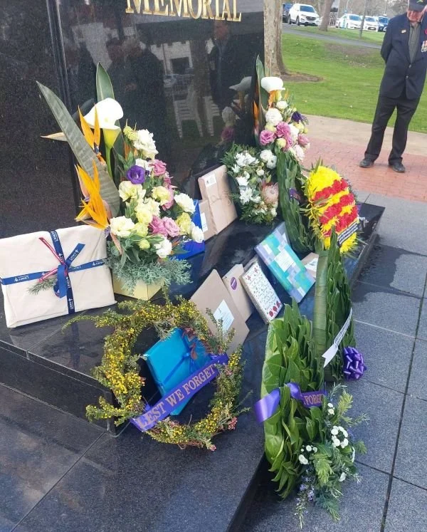 Memorial in a park with flowers, wreaths, and messages honoring someone, with a person standing nearby.