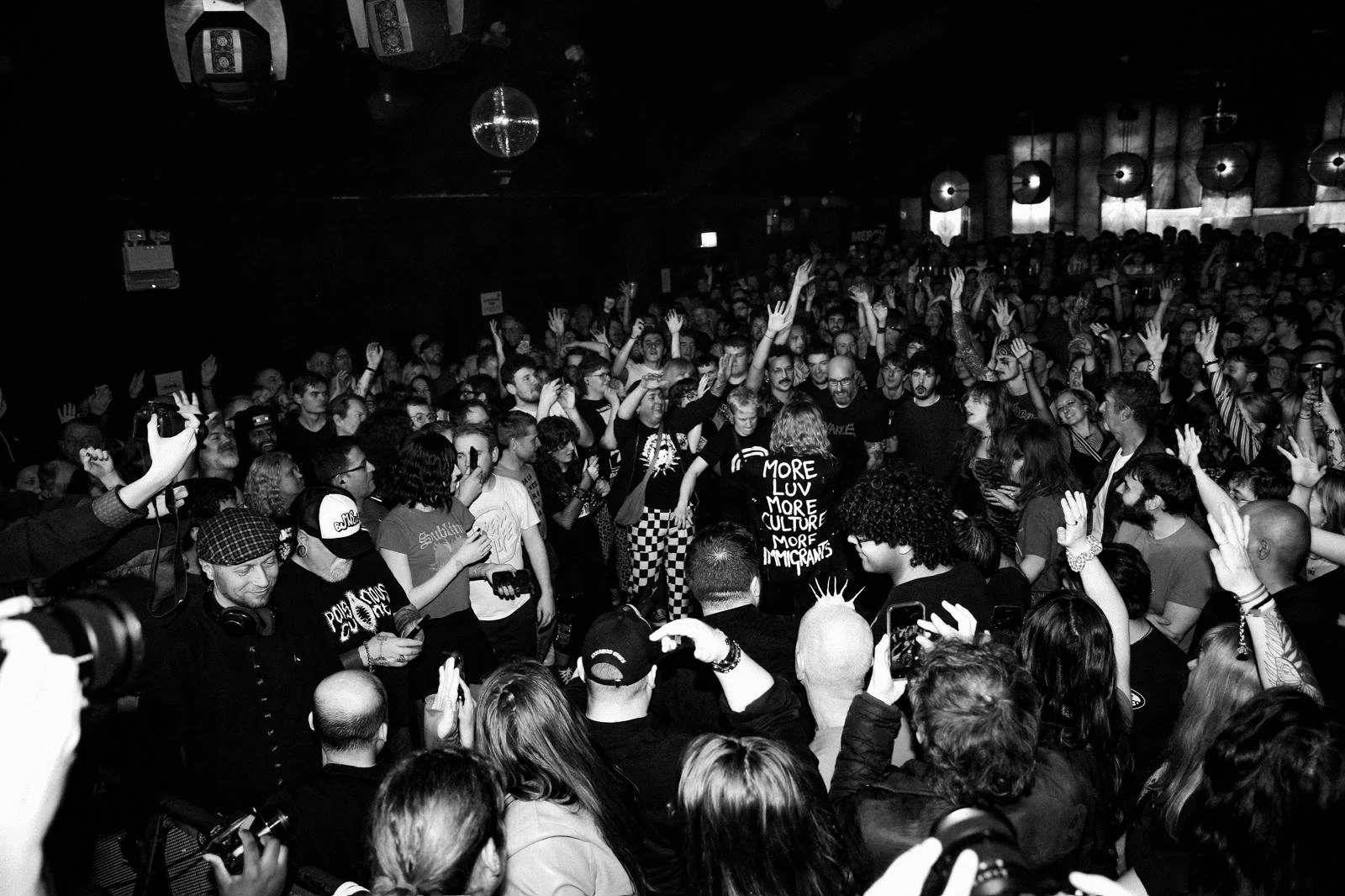 Black and white photo of a crowded concert or event with many people raising hands and taking pictures.