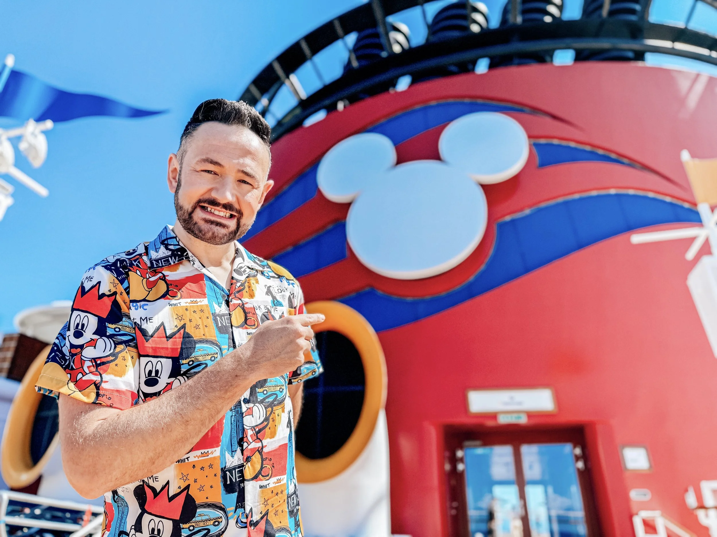 Ben in colorful Mickey Mouse shirt pointing at a Disney-themed building with Mickey Mouse head decorations