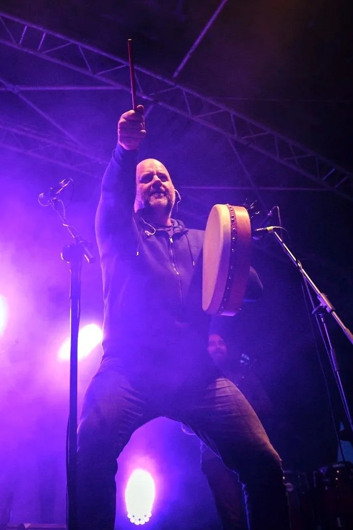 Musician playing hand drum on stage with purple lighting.