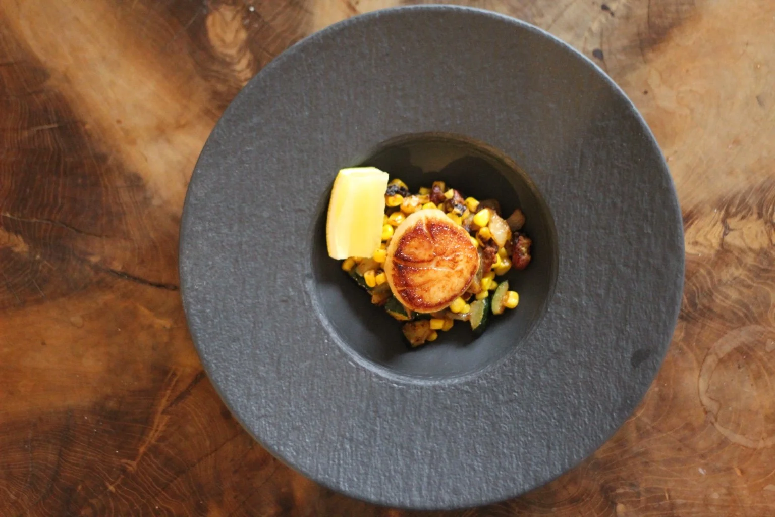 Seared scallop with corn and vegetables, plated for a tasting menu.