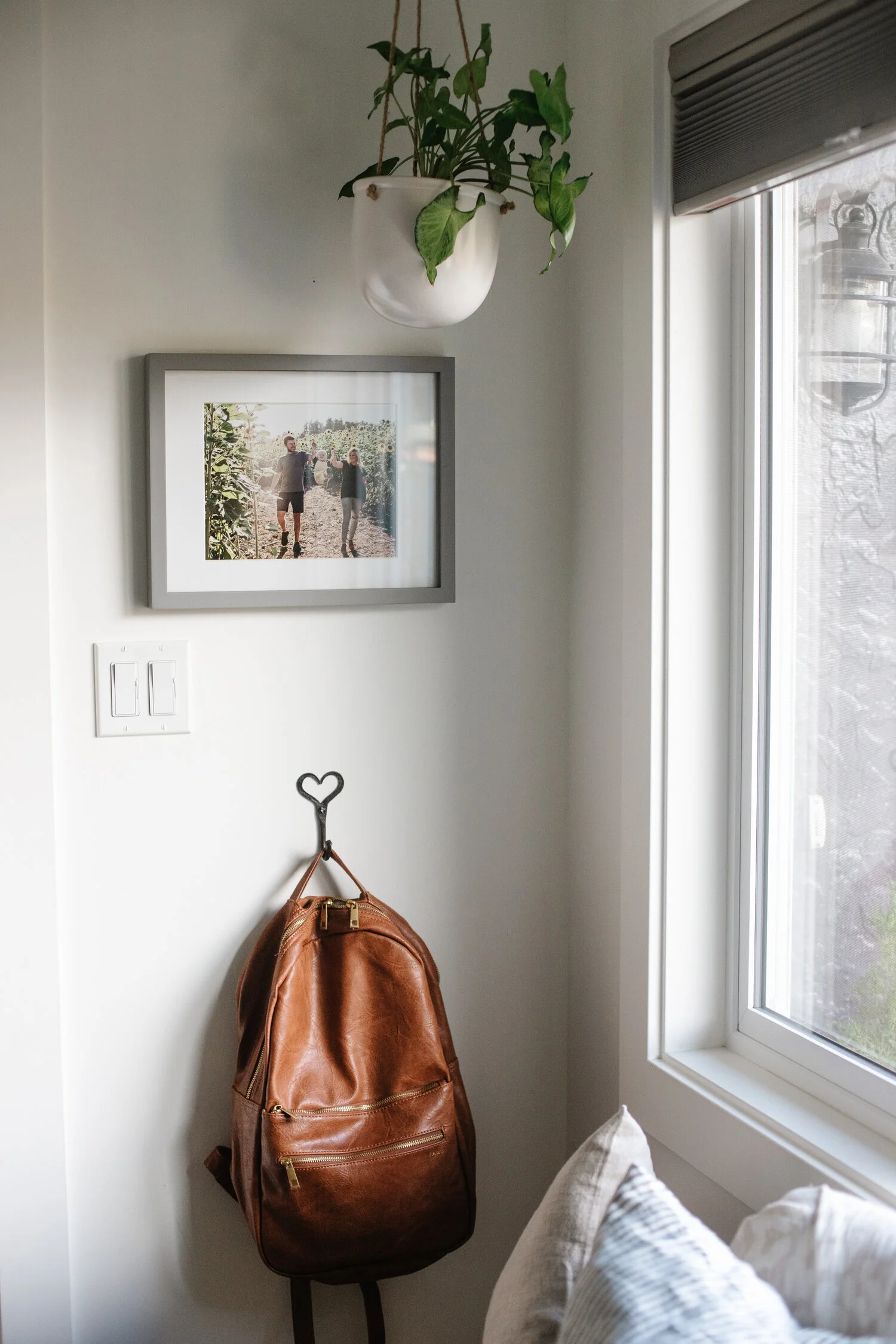 A brown faux leather backpack hanging on a hook, next to a window, in the corner of an office space.