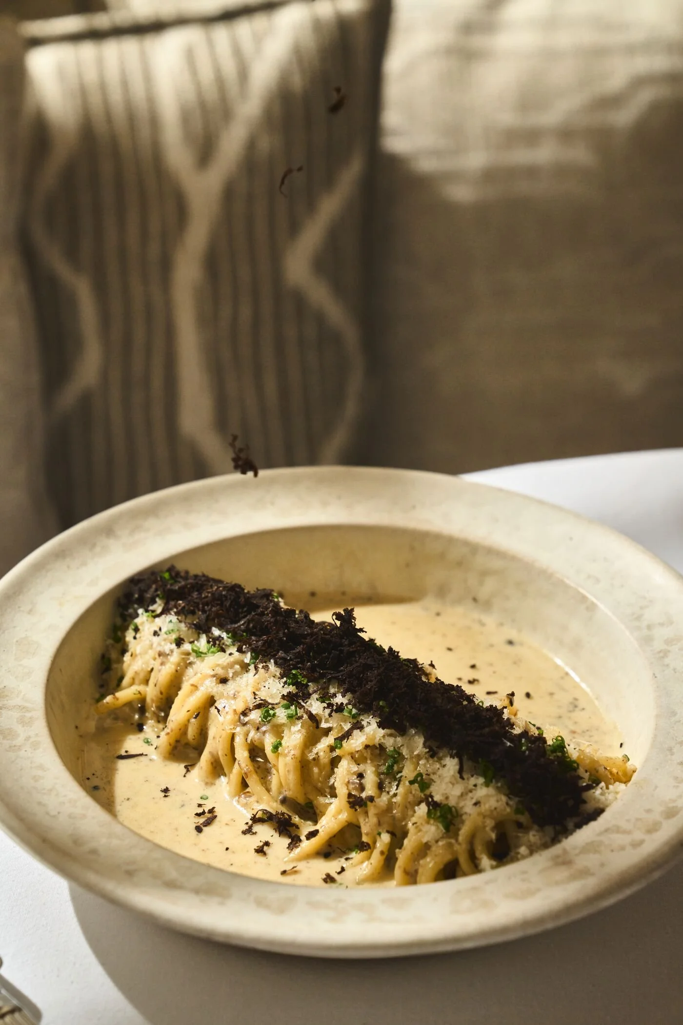 A bowl of creamy pasta topped with shredded cheese, chopped herbs, and black sesame seed, with shredded seaweed on top.