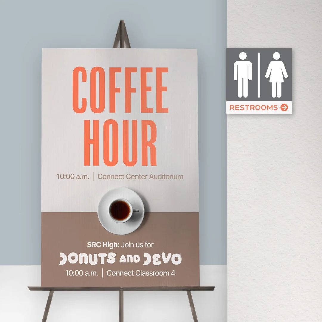 Sign advertising 'Coffee Hour' at 10:00 a.m. in the Connect Center Auditorium, featuring 'Donuts and Devo' in Connect Classroom 4. A cup of coffee is shown on the sign. Restroom sign with male and female icons on the wall to the right.