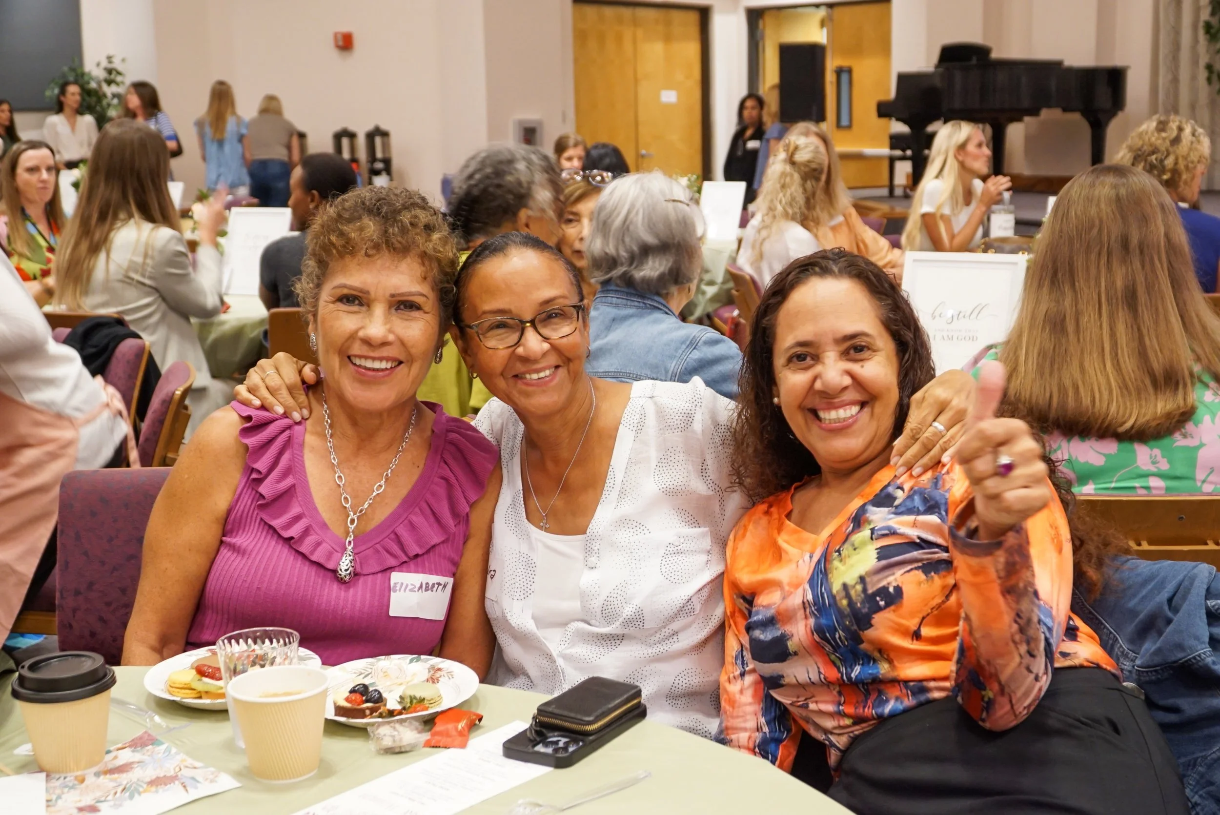 Five women standing in front of a wall, holding diapers and baby supplies, with boxes of additional supplies on the ground.