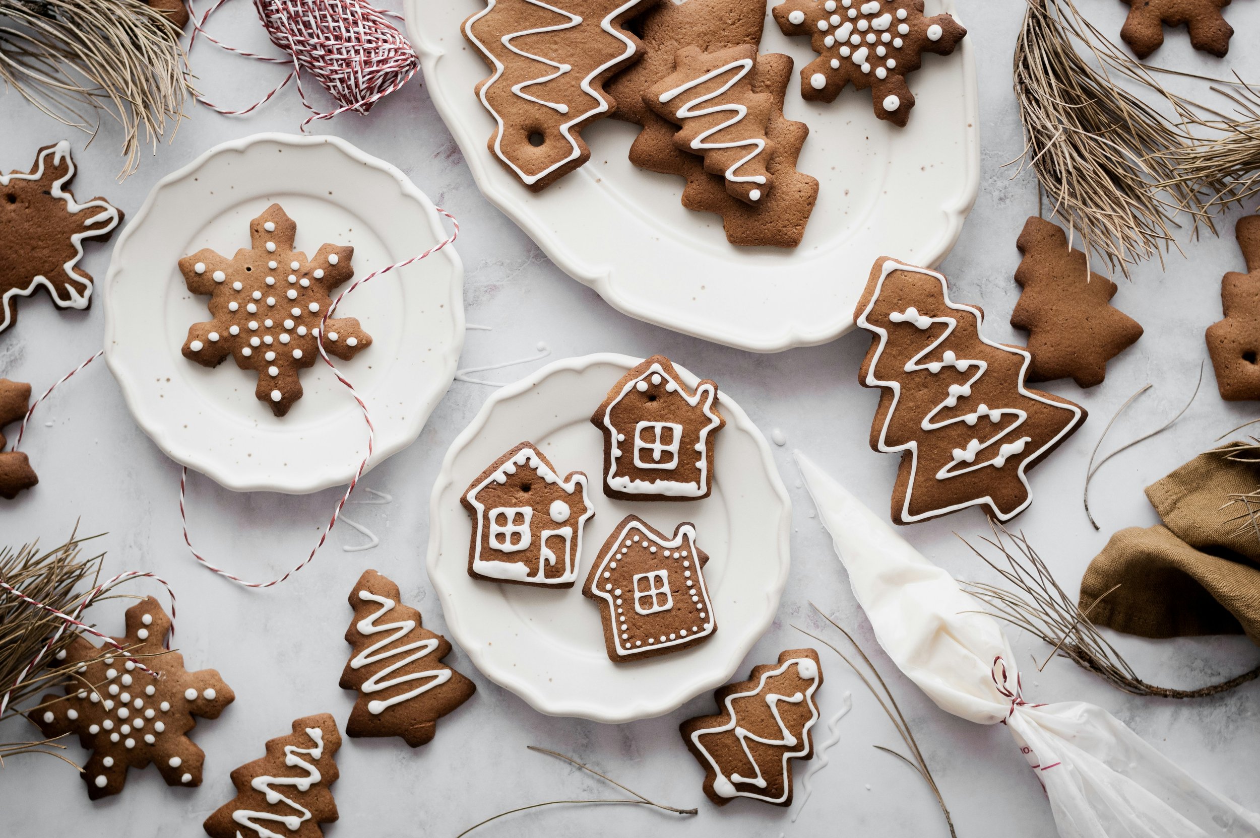 Decorated Christmas cookies on a wooden board with blurred Christmas ornaments and tree in the background.