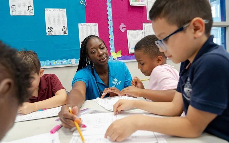 A teacher assisting young students with their schoolwork in a classroom.