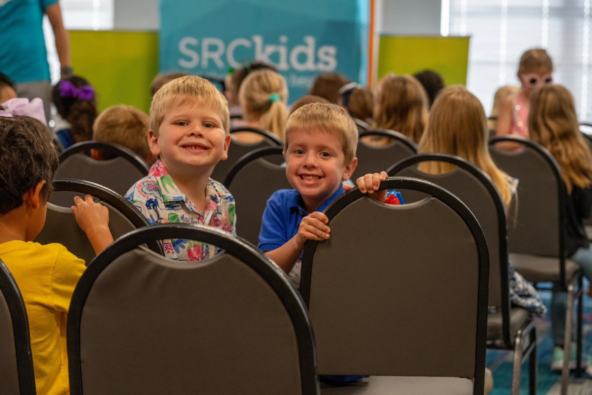 A man with glasses, a bald head, and a goatee speaking at a podium, wearing a dark blazer and white shirt, making a point with his hand, with a large book on the podium.