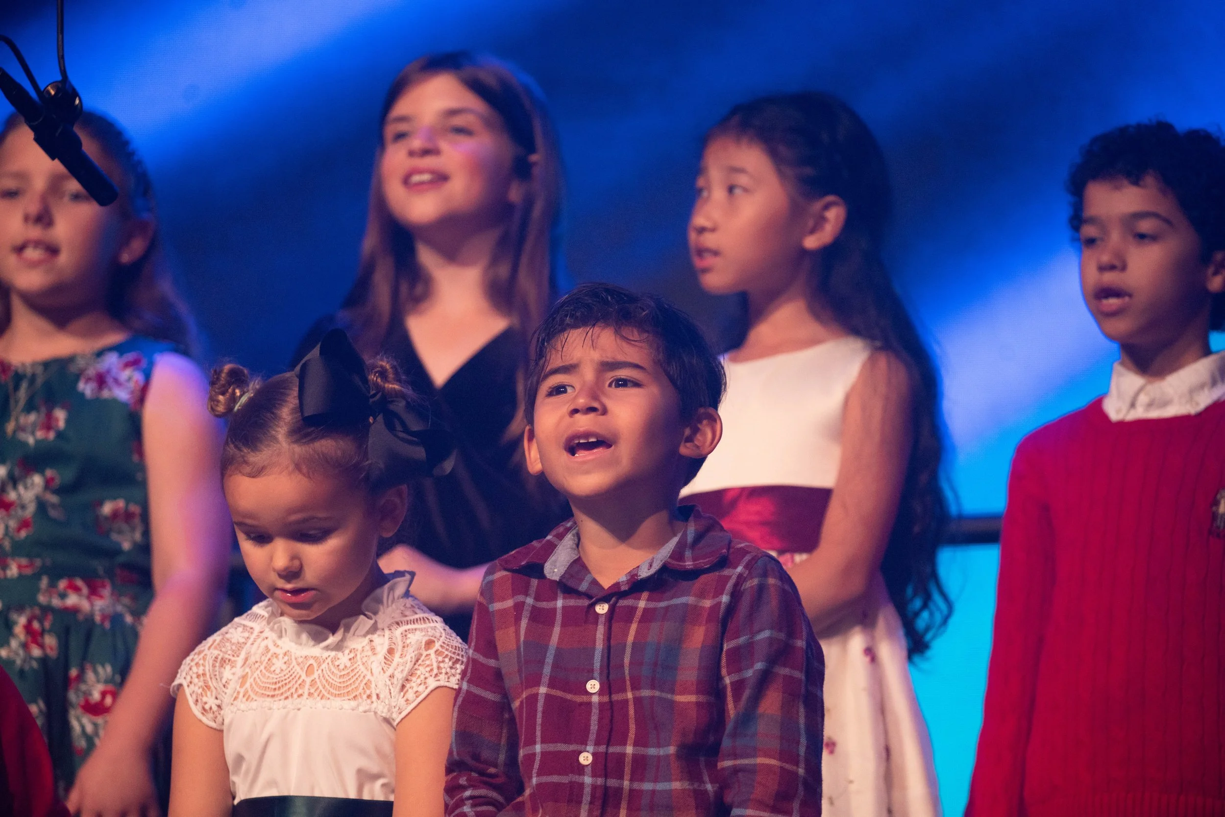 Children singing on stage, dressed in festive clothes, performing in a choir concert.