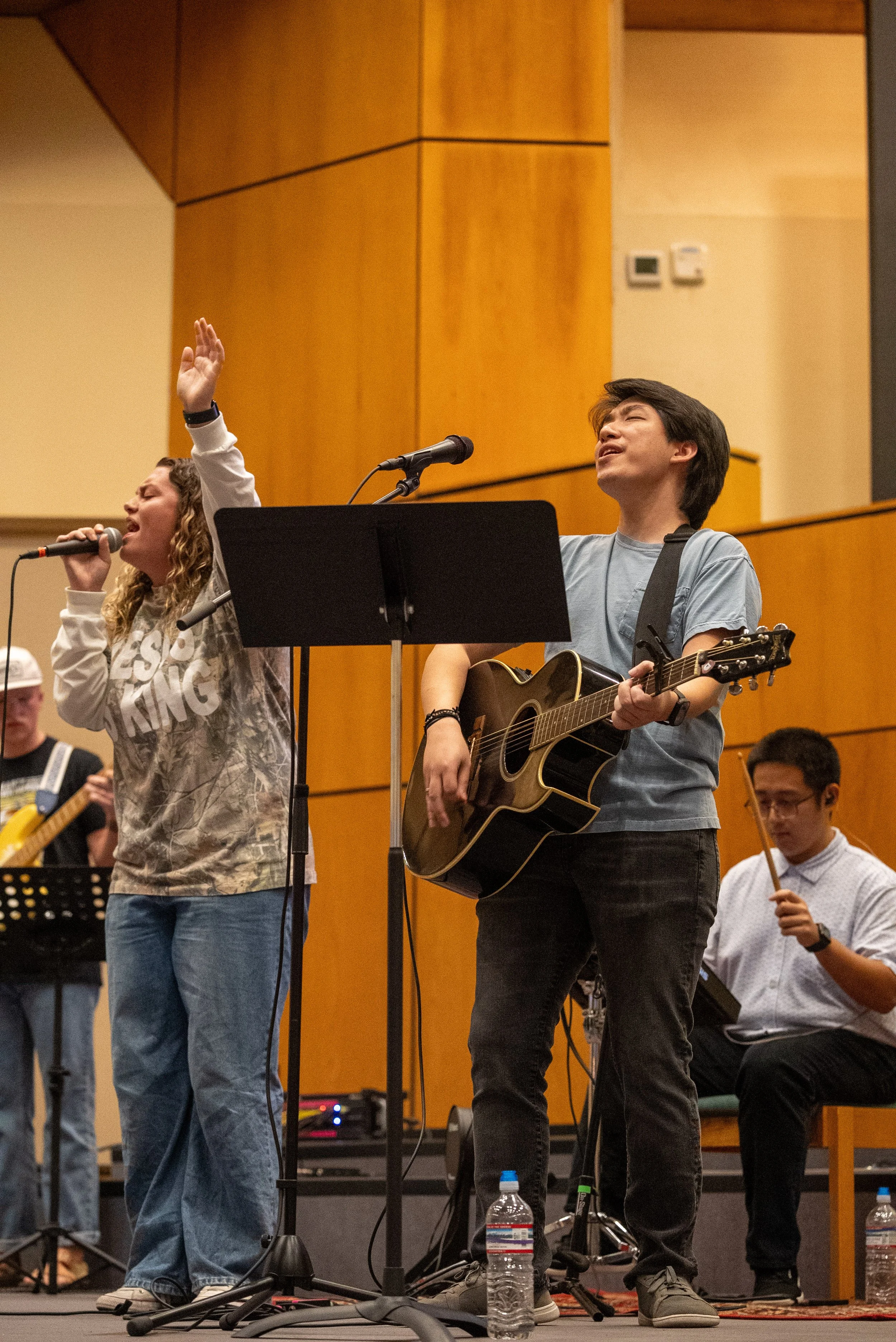 A smiling young man wearing an orange T-shirt with the text 'Spanish River Church' stands near a glass door that has similar signage. He has a black lanyard around his neck and a watch on his wrist.