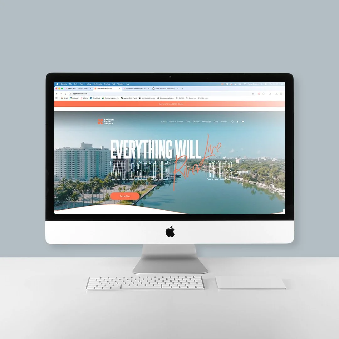 An Apple iMac computer with a website displayed on the screen, showing a river scene with buildings and trees, and text that says 'Everything will live where the river goes'.