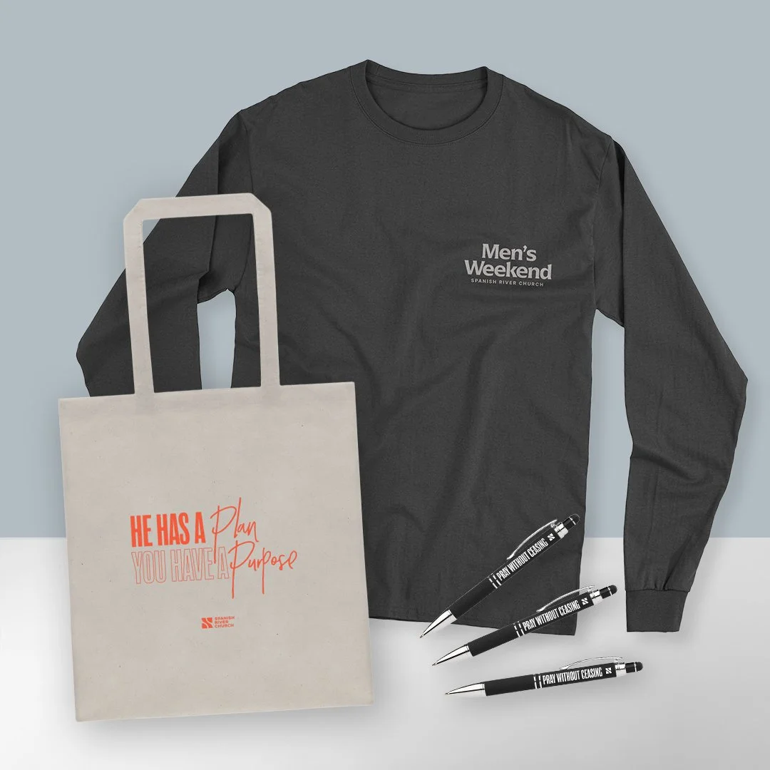 A black long-sleeve shirt with white text that says 'Men's Weekend' and 'Spanish River Church,' three black pens with the words 'Pray Without Ceasing,' and a beige tote bag with red and light gray text that says 'He Has a Plan You Have a Purpose.'
