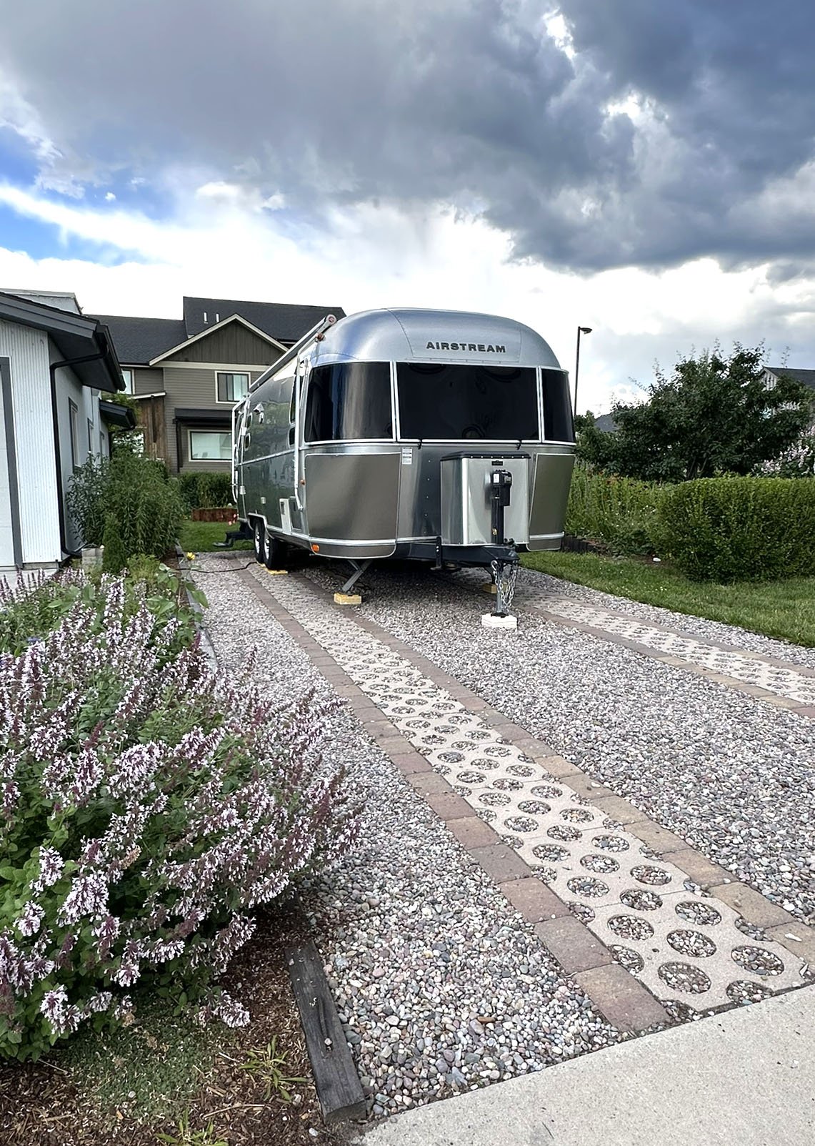 Permeable trailer parking bordered by gravel and wood edging, with pink catmint softening the driveway beside a garage.