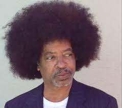 Man with large afro hairstyle wearing a dark blazer, looking to the side