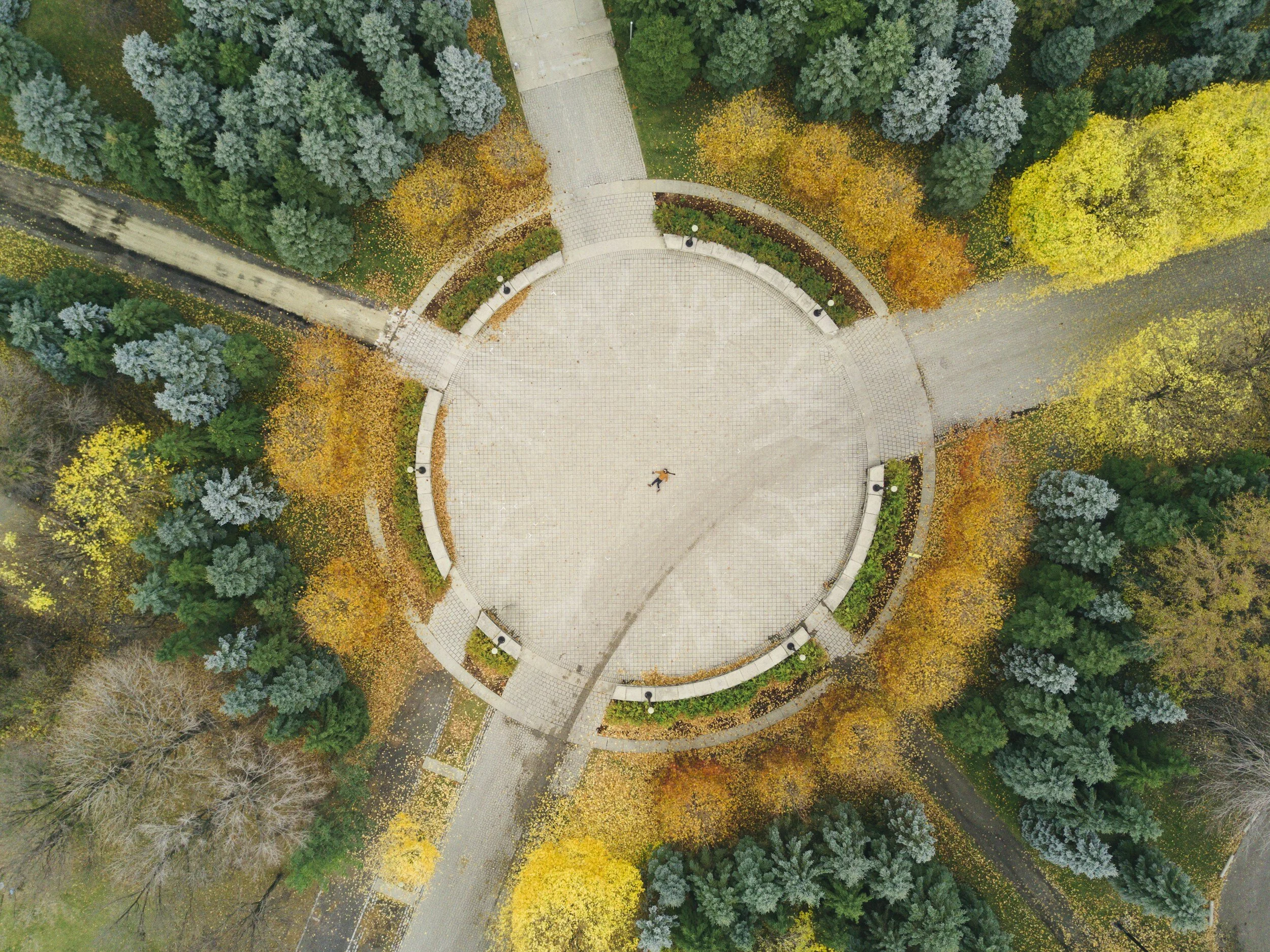 An aerial view of a park with a circular paved area surrounded by autumn trees and pathways.